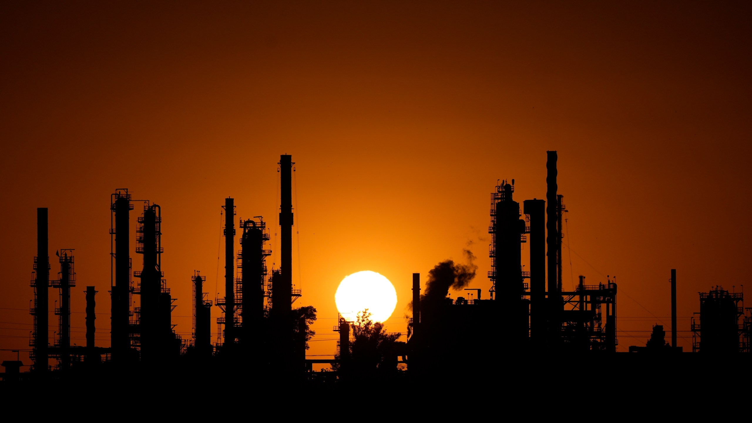 An oil refinery is silhouetted against the setting sun