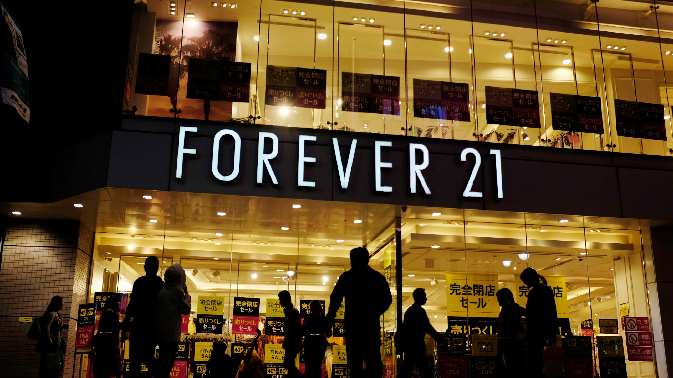 FILE - Shoppers walk by a Forever 21 clothing store, Thursday, Oct. 24, 2019, in Tokyo, as the liquidation sale signs are posted on the storefront. (AP Photo/Kiichiro Sato, file)