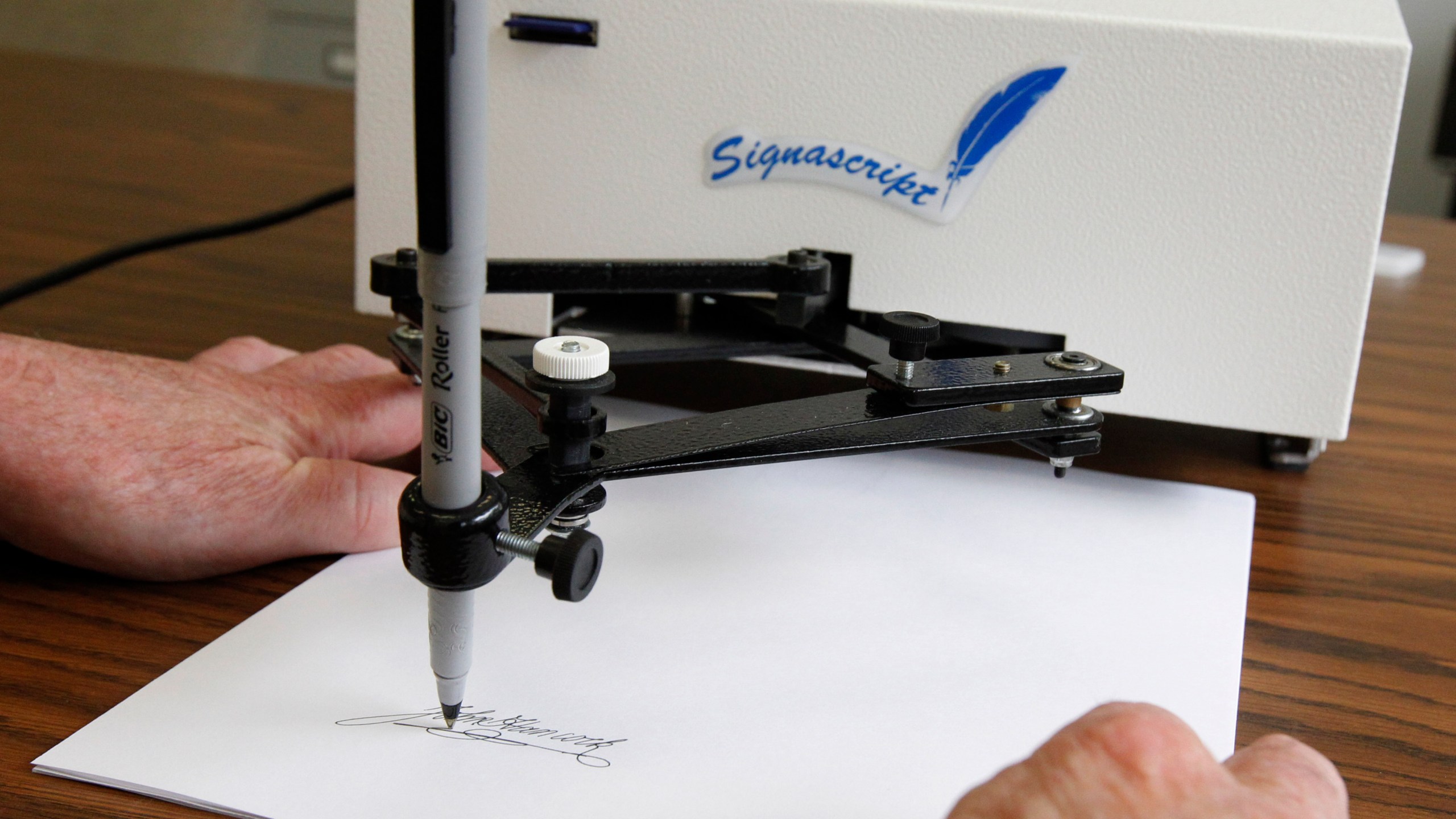 Damilic Corp. president Bob Olding anchors a sheet of paper as the Atlantic Plus, the Signascript tabletop model autopen, produces a signature at their Rockville, Md., office, June 13, 2011. (AP Photo/Manuel Balce Ceneta, File)
