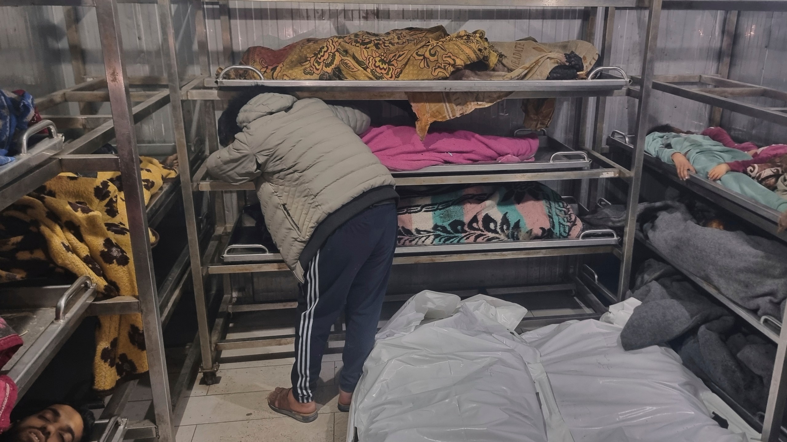 A man mourns over the body of a child, lying among other victims at the hospital morgue, following Israeli airstrikes in Khan Younis, southern Gaza Strip, Tuesday, March 18, 2025. (AP Photo/Mohammad Jahjouh)