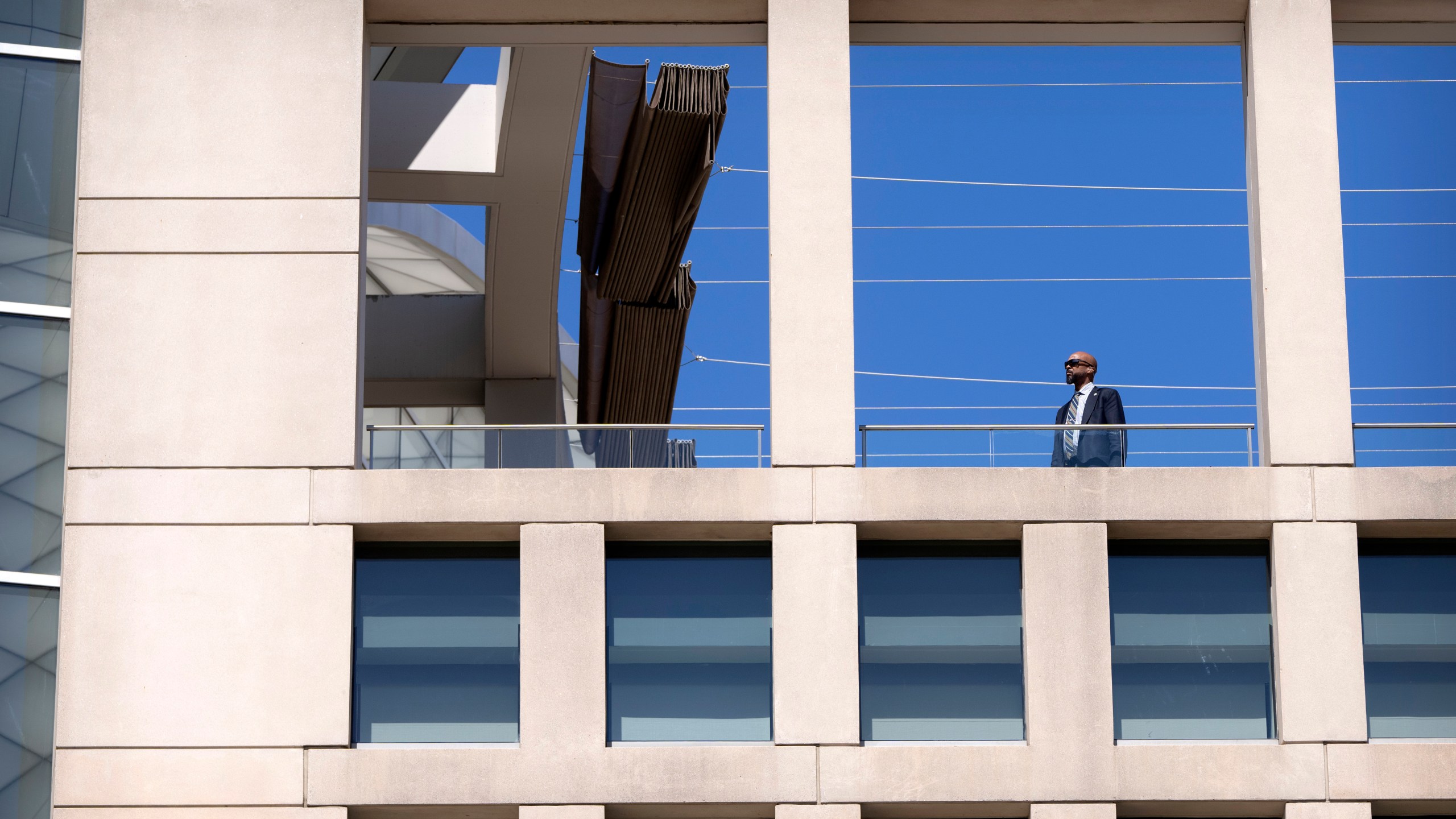 A man wearing an earpiece stands on a balcony at the headquarters of the United States Institute of Peace, Tuesday, March 18, 2025, in Washington. (AP Photo/Mark Schiefelbein).