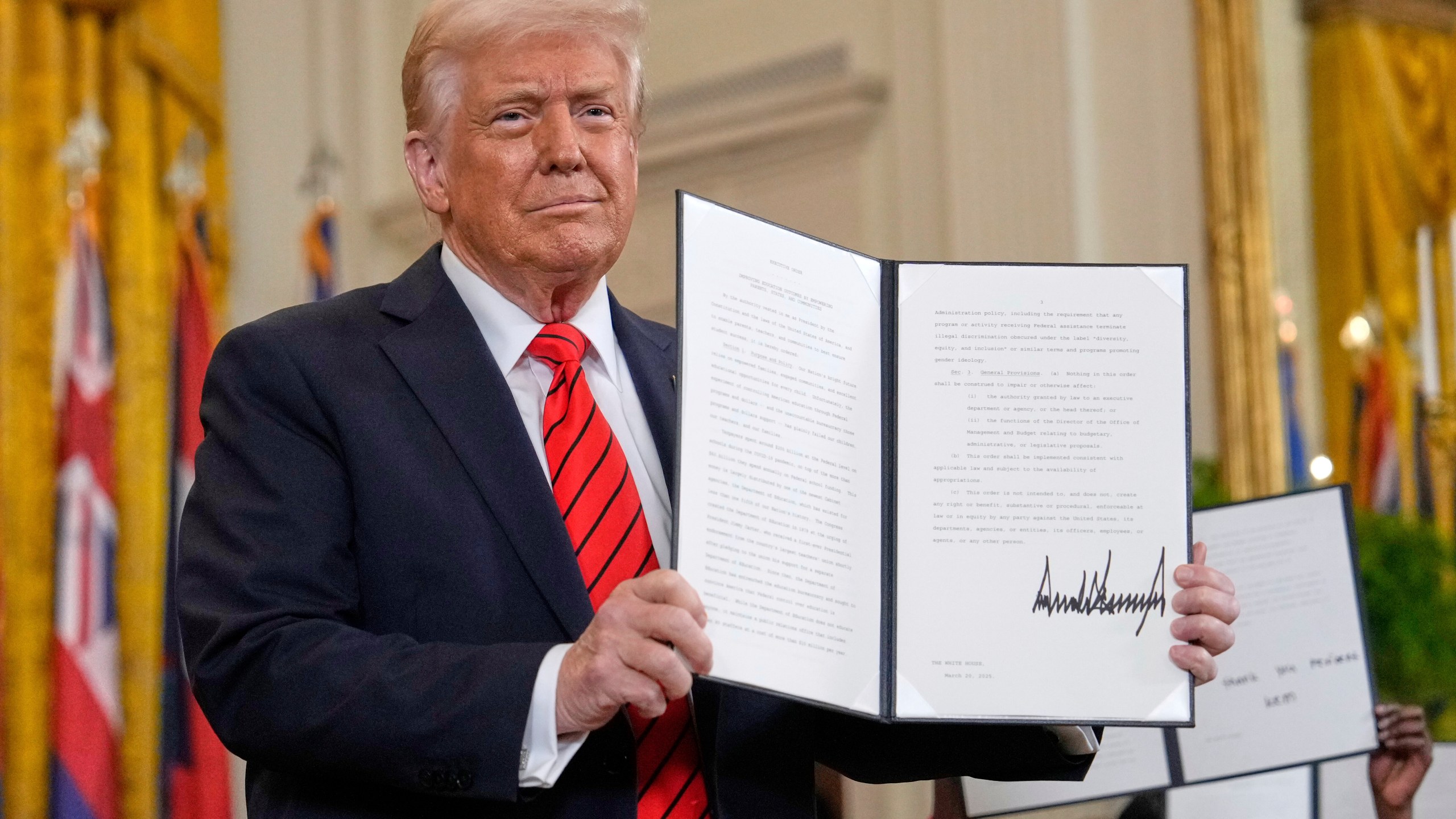 President Donald Trump holds up a signed executive order at an education event in the East Room of the White House in Washington, Thursday, March 20, 2025. (AP Photo/Ben Curtis)