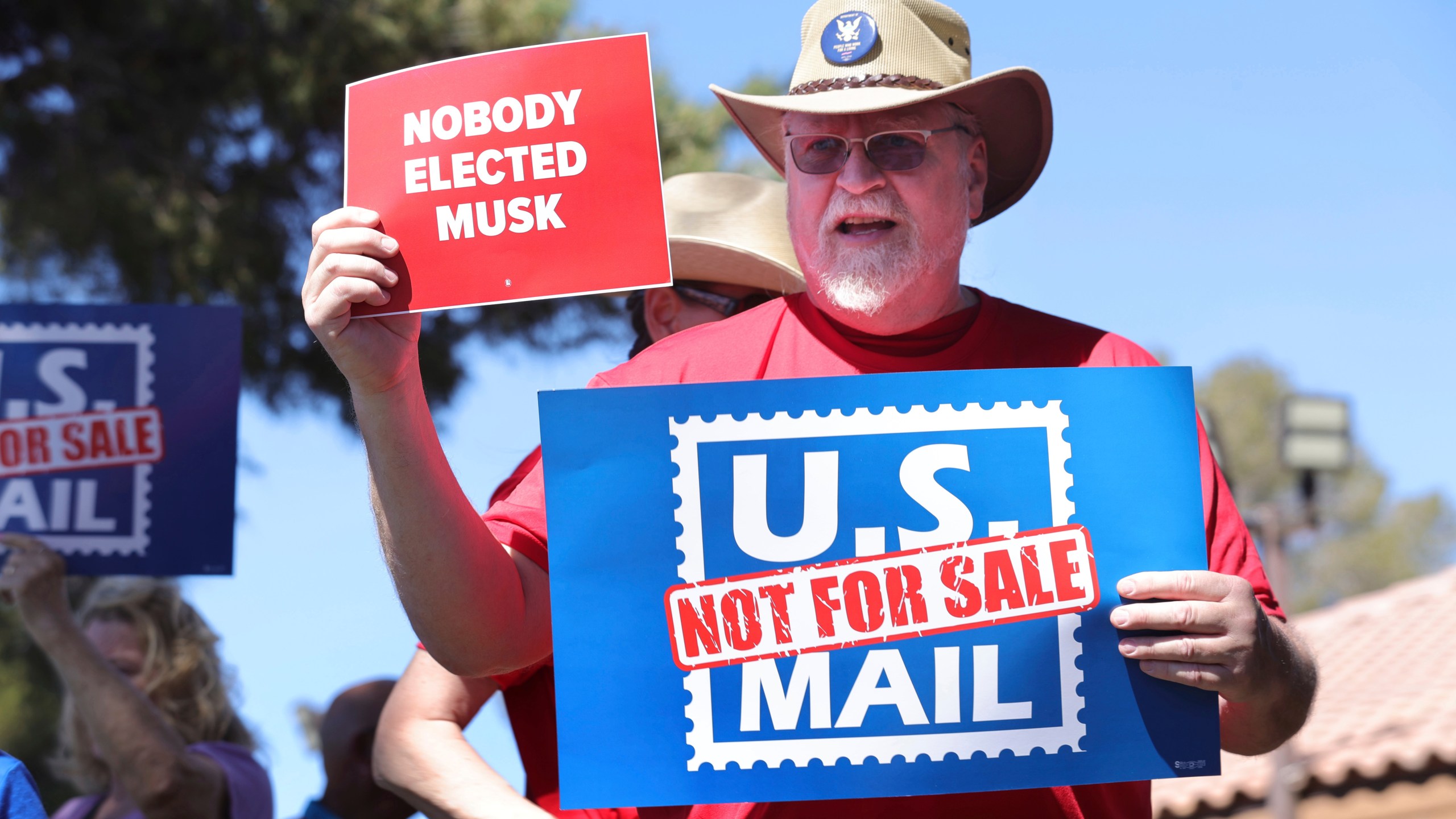FILE - Letter carrier Fred Moss holds up signs during a protest, part of a national series of rallies against the Trump administration's plans to privatize or restructure the U.S. Postal Service, Sunday, March 23, 2025, in Las Vegas. (Steve Marcus/Las Vegas Sun via AP, File)