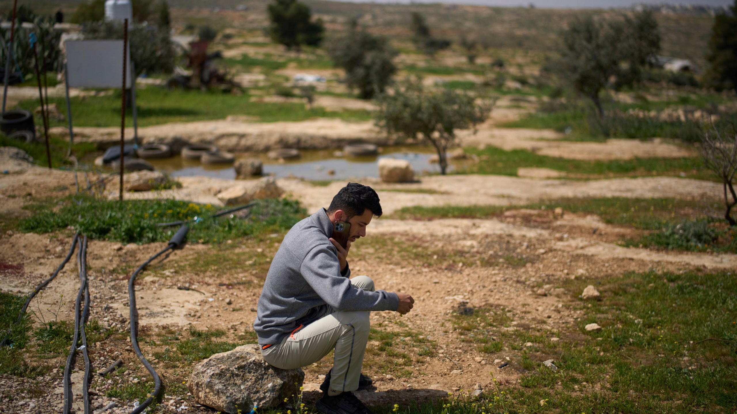 Basel Adra, one of the directors of the Oscar winner documentary "No Other Land", speaks on the phone as he sits in an area near the house of Palestinian co-director Hamdan Ballal, in the village of Susiya in Masafer Yatta, south Hebron hills Tuesday, March 25, 2025. (AP Photo/Leo Correa)
