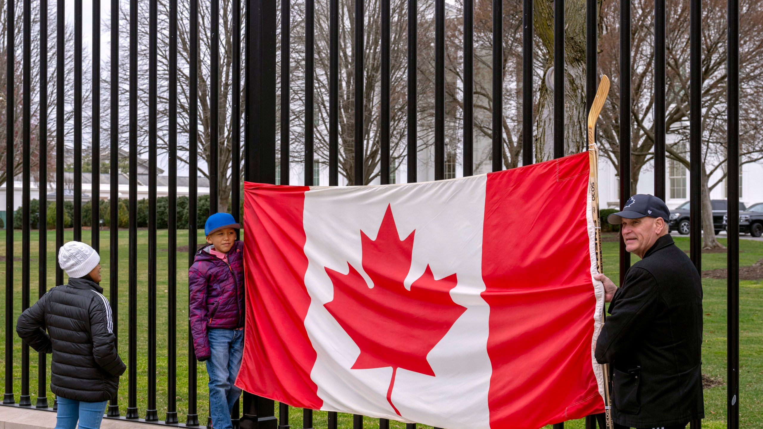 FILE - Toronto residents Douglas Bloomfield, from right, his son Phoenix and wife Ame, who are on vacation in Washington, hold a Canadian flag and an ice hockey stick to show their support for Canada regarding trade tariffs in front of the White House in Washington, March 13, 2025. (AP Photo/Ben Curtis, File)