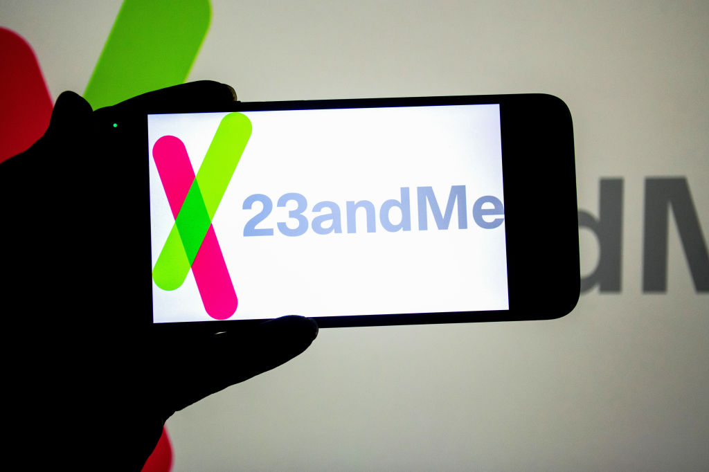 , a 23andMe logo seen displayed on a smartphone and in the background.