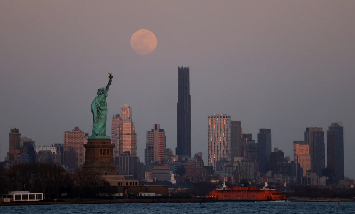 The full moon rises above the skyline of New York City