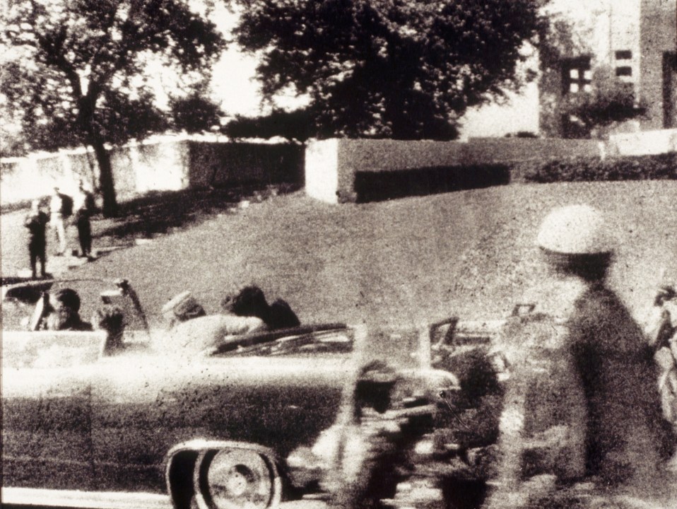 Grainy black and white photo image of Kennedy leaning over in his car