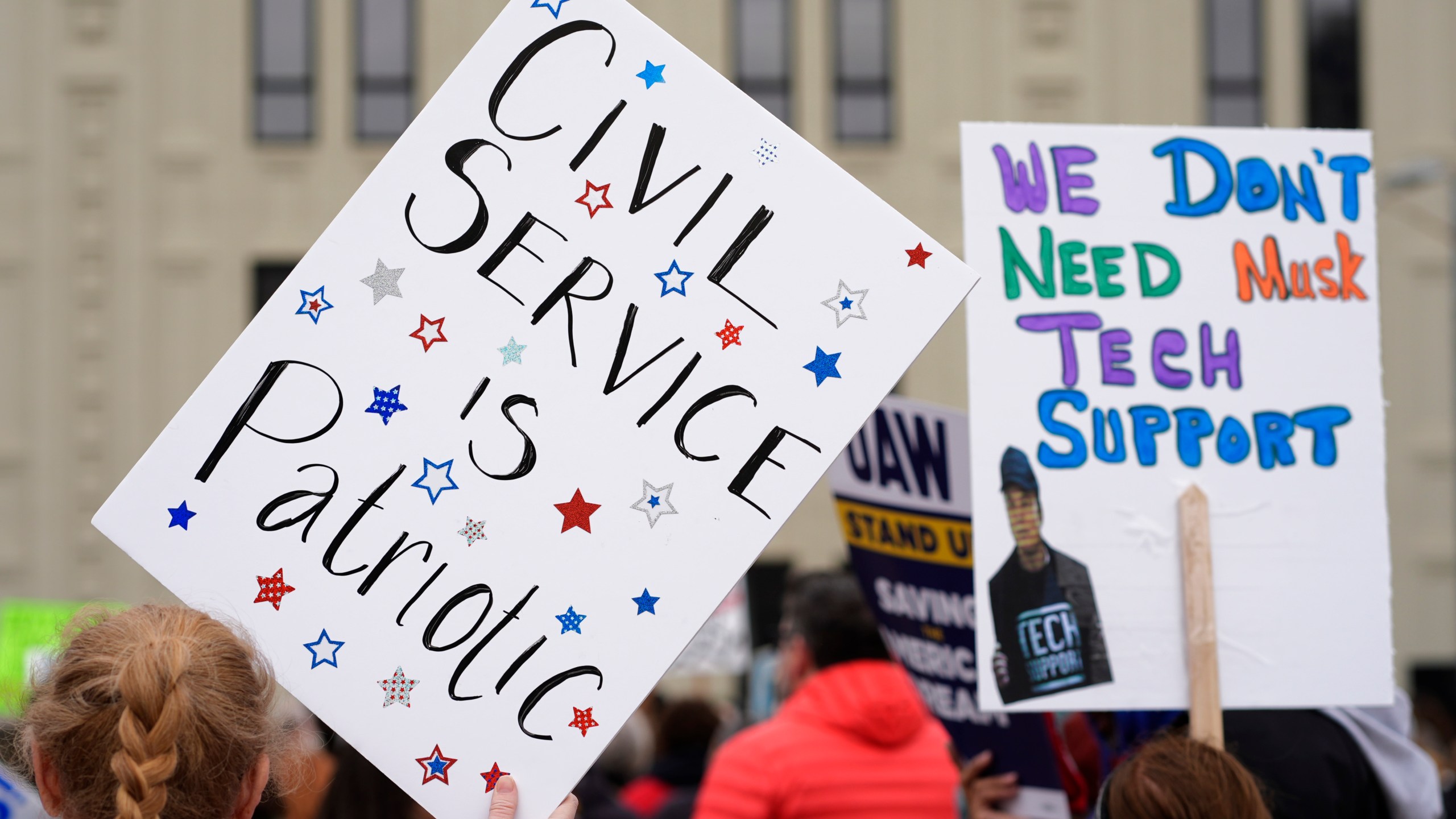 People hold signs at a rally supporting federal workers outside the IRS regional office Saturday, March 15, 2025, in Kansas City, Mo. (AP Photo/Charlie Riedel)