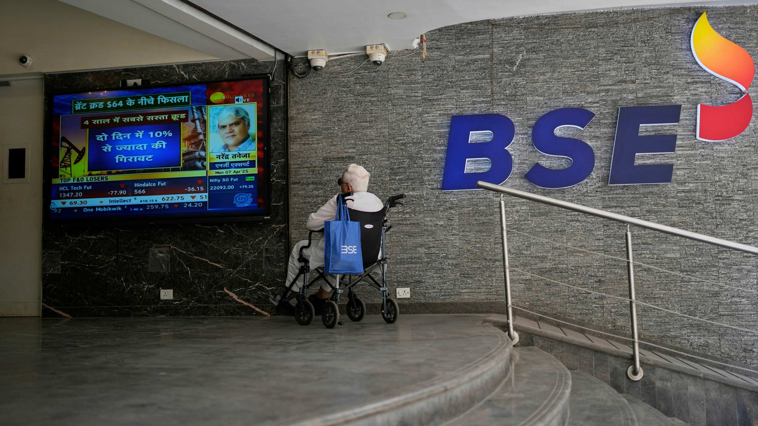 A man sits on a wheelchair and watches a live screen outside Bombay Stock Exchange (BSE) building in Mumbai, India, Monday, April 7, 2025. (AP Photo/Rajanish Kakade)
