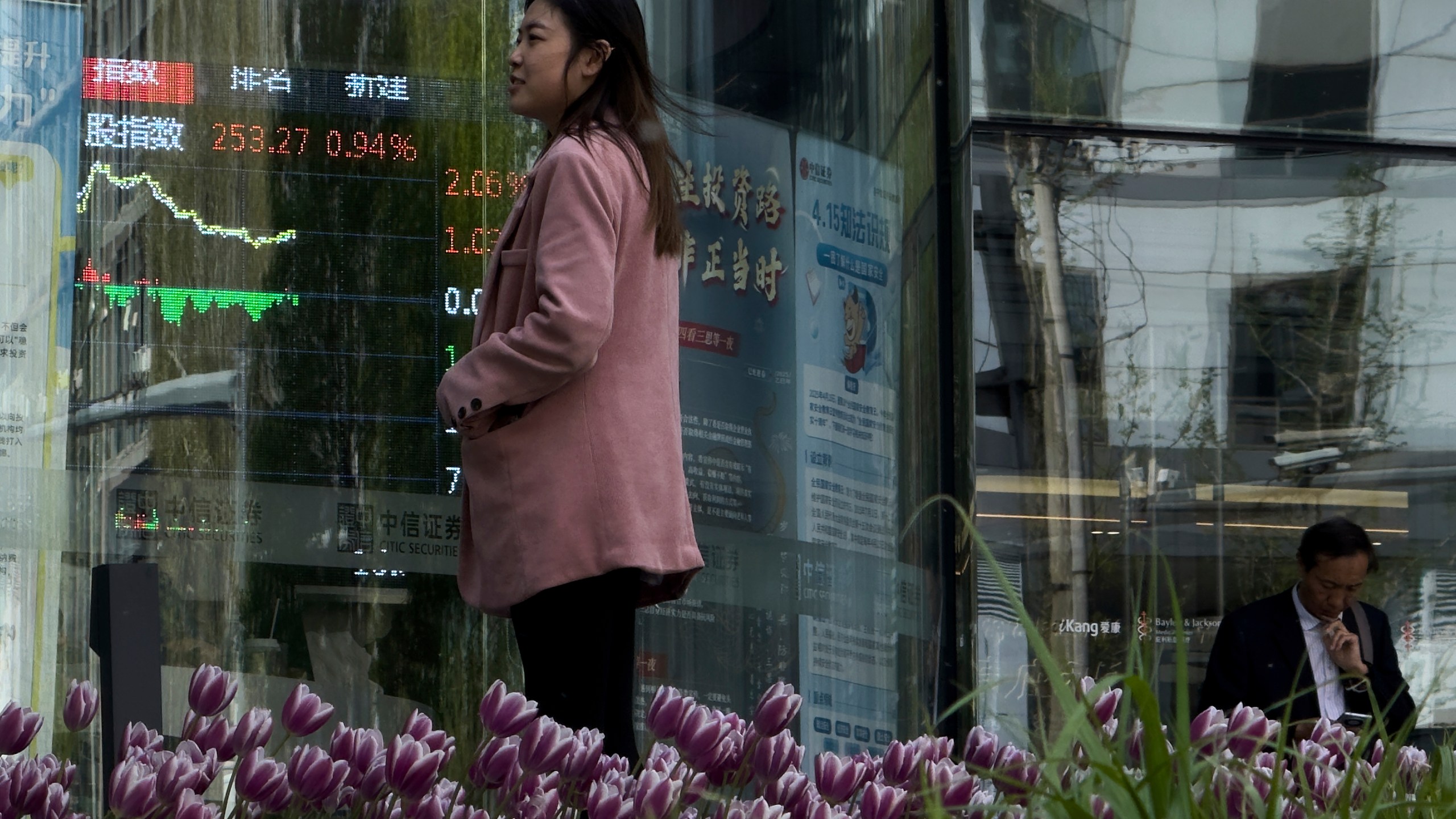 People stand outside a brokerage house as an electronic board displays shares trading index in the Central Business District, in Beijing, Thursday, April 10, 2025. (AP Photo/Andy Wong)