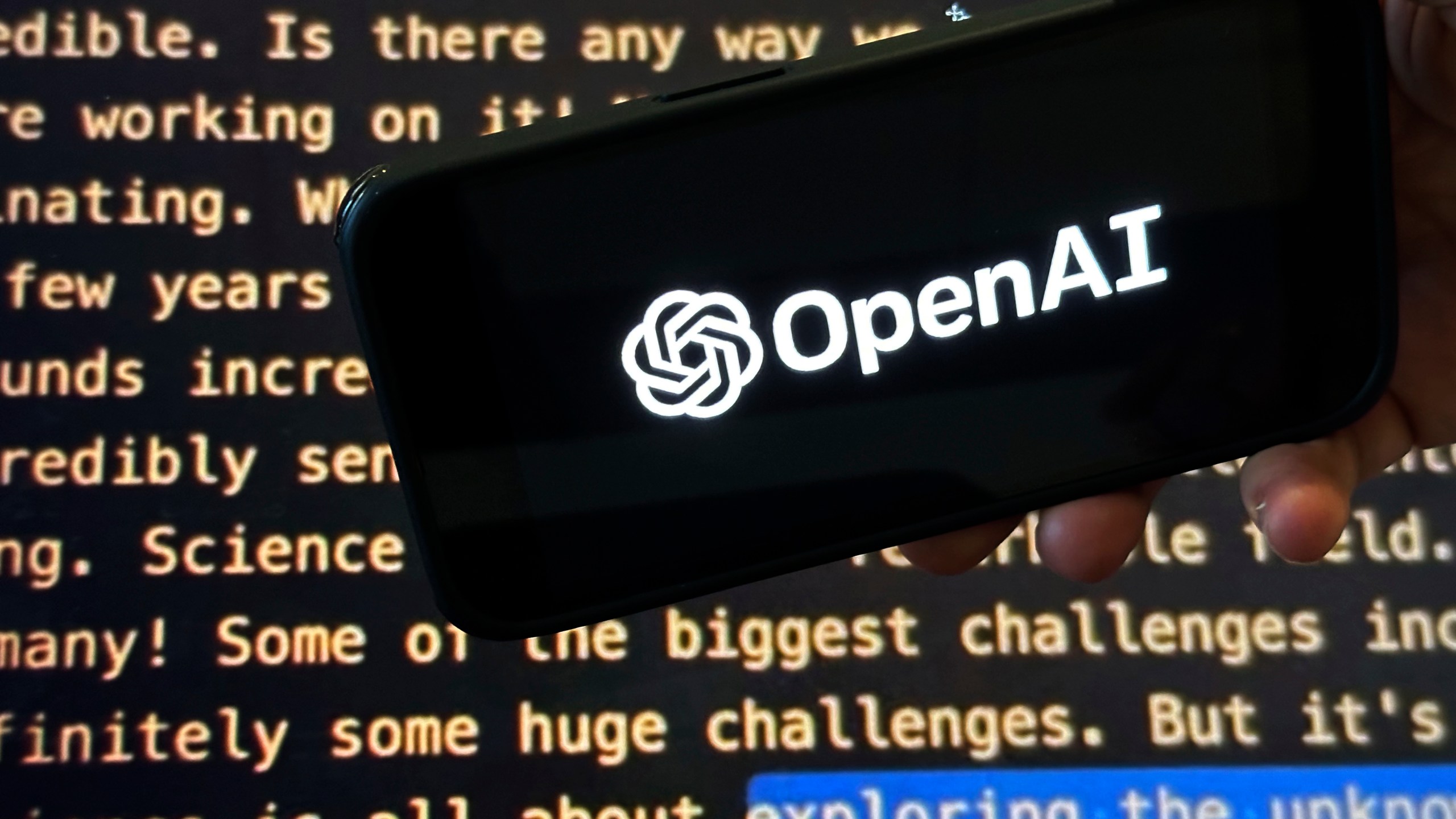 FILE - The OpenAI logo appears on a mobile phone in front of a screen showing part of the company website in this photo taken on Nov. 21, 2023 in New York. (AP Photo/Peter Morgan, File)