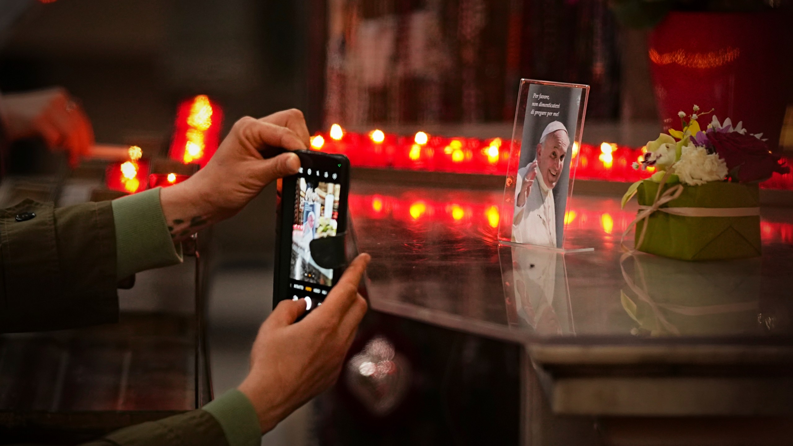 A woman takes a picture of a photograph of the late Pope Francis, that reads "Please, don't forget to pray for me" during a mass in his memory at the Chiesa di Santo Spirito in Sassia outside the Vatican, Thursday, April 24, 2025. (AP Photo/Andreea Alexandru)