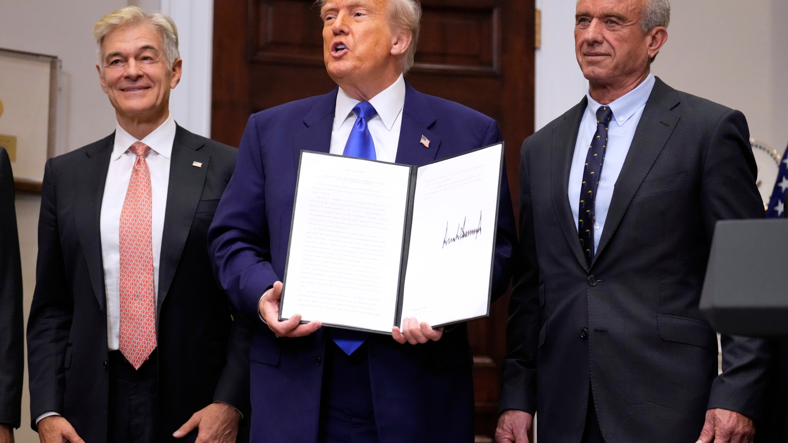 President Donald Trump, with Dr. Mehmet Oz, Administrator of the Centers for Medicare & Medicaid Services, left, and Health and Human Services Secretary Robert F. Kennedy Jr., right, holds an executive order related to drug prices, in the Roosevelt Room of the White House in Washington, Monday, May 12, 2025, in Washington. (AP Photo/Mark Schiefelbein)