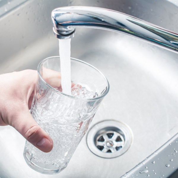 A person holding a glass at a sink to get water