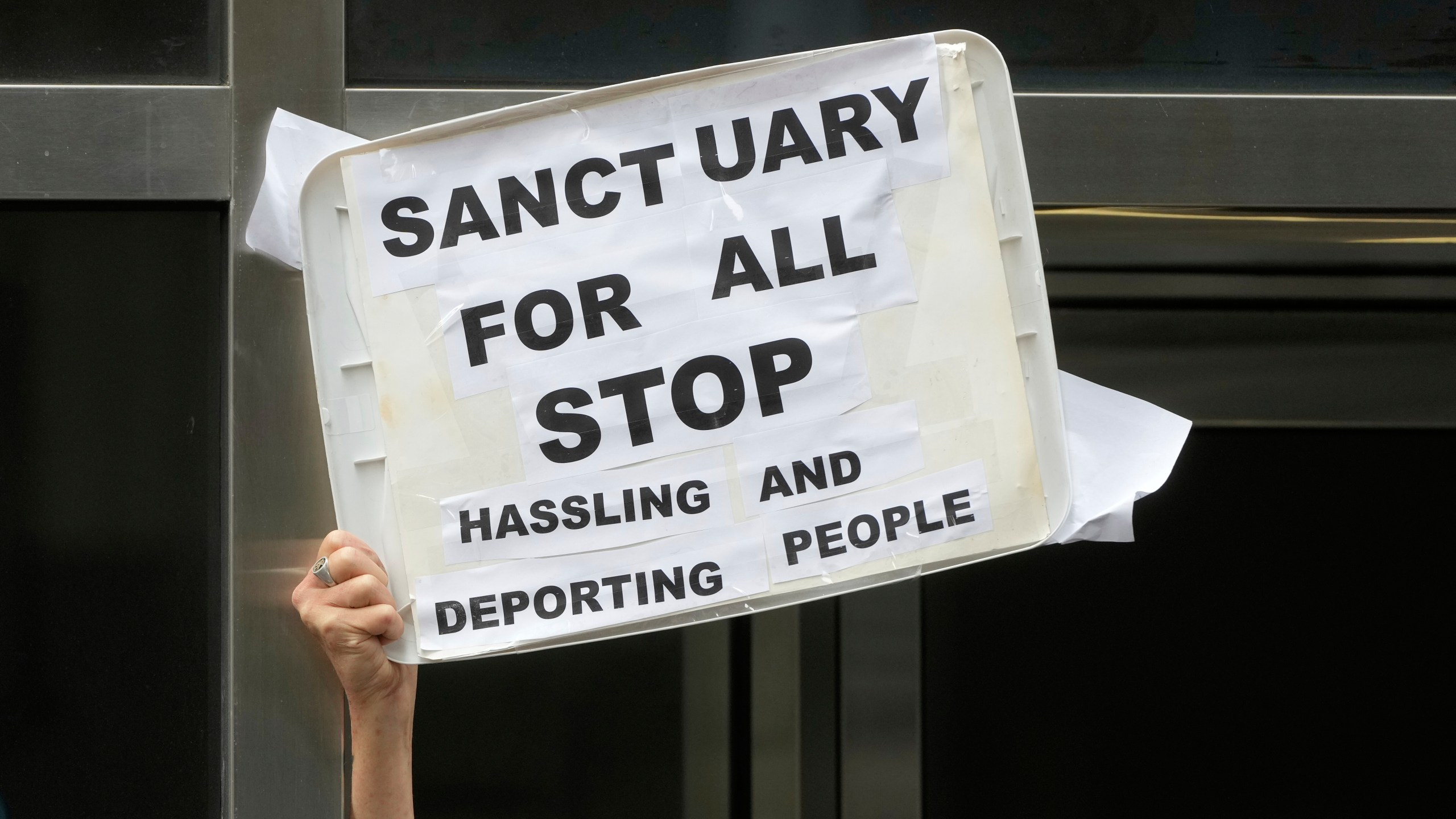 A person holds up a sign during a news conference and rally by immigrant justice organizations and advocates protesting ICE arrests in San Francisco, Wednesday, May 28, 2025. (AP Photo/Jeff Chiu)