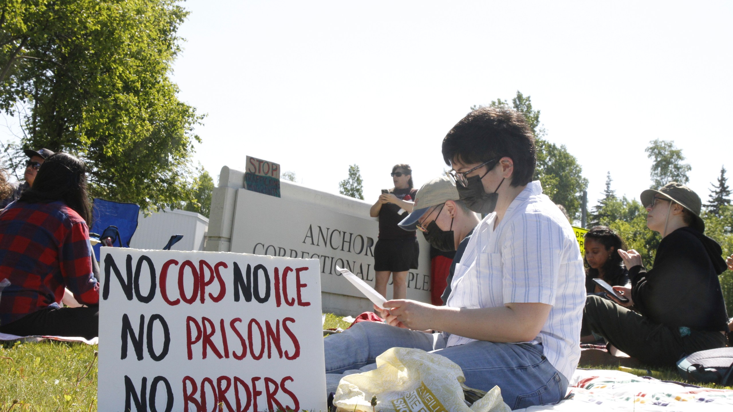 Demonstrators sit on the lawn of the Anchorage Correctional Complex Thursday, June 12, 2025, in Anchorage, Alaska, to protest the detainment of about 40 people being held there under the custody of the Immigration and Customs Enforcement federal agency. (AP Photo/Mark Thiessen)