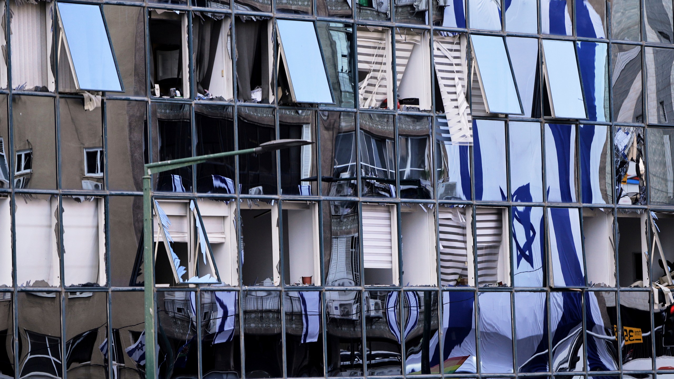 The Israeli flag is reflected in the windows of a damaged building in Ramat Gan, Israel, two days after it was hit by a missile launched from Iran, Saturday, June 21, 2025. (AP Photo/Ohad Zwigenberg)