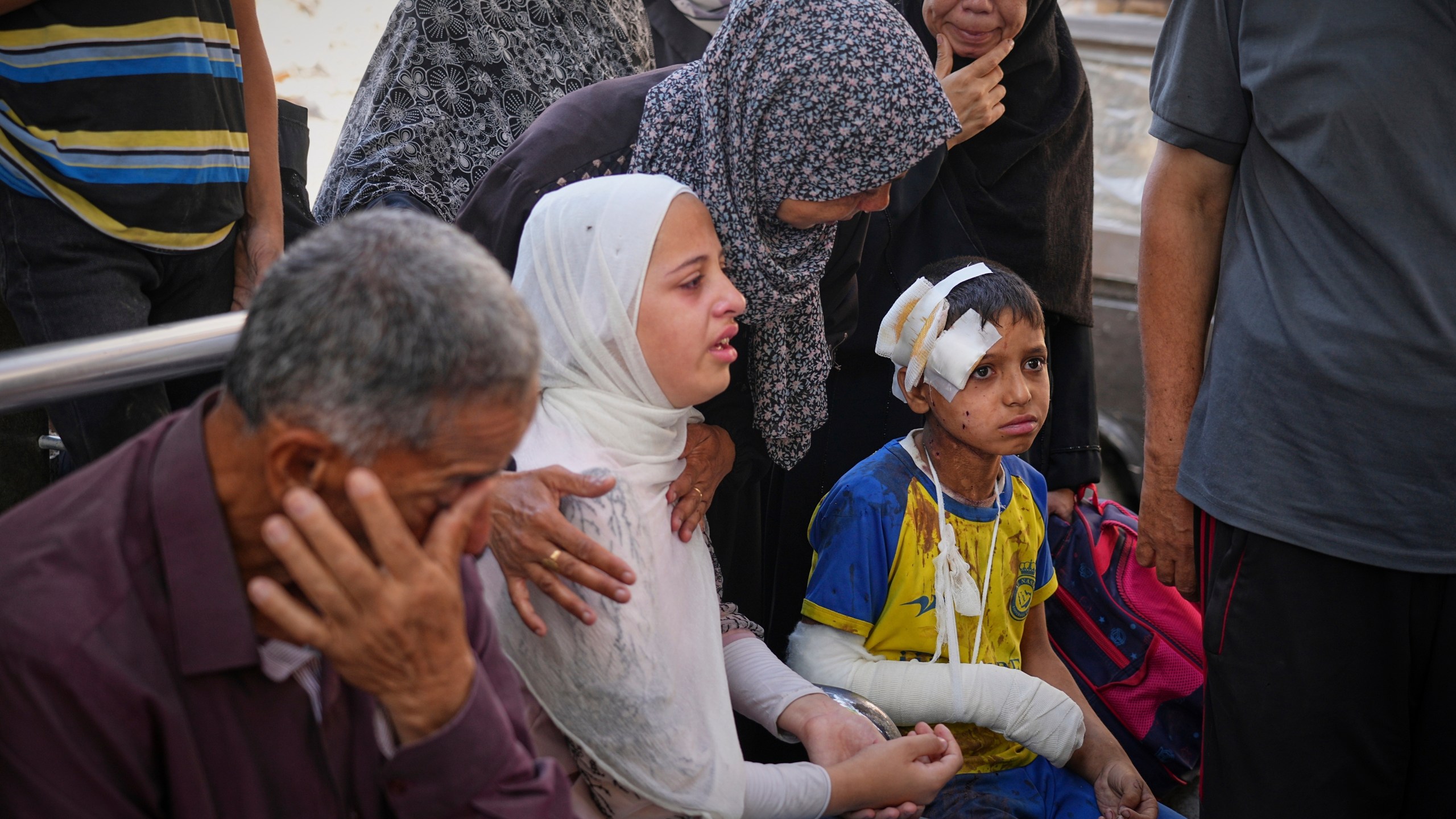 a man wipes tears as a woman cries next to an injured boy with bandages
