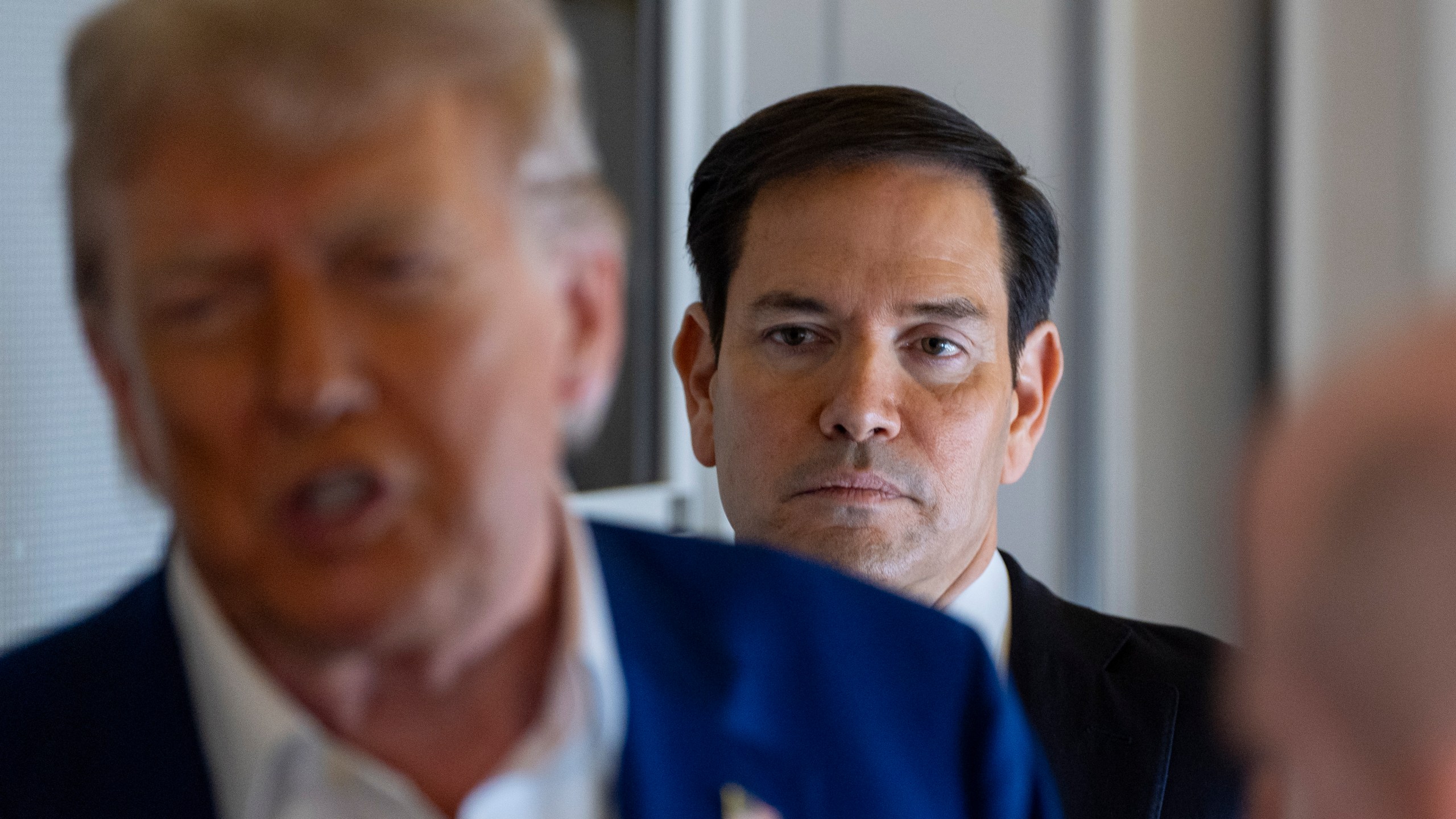Secretary of State Marco Rubio stands behind as President Donald Trump speaks with reporters on Air Force One while in flight from Joint Base Andrews, Md., to Amsterdam, Netherlands, Tuesday, June 24, 2025. (AP Photo/Alex Brandon)