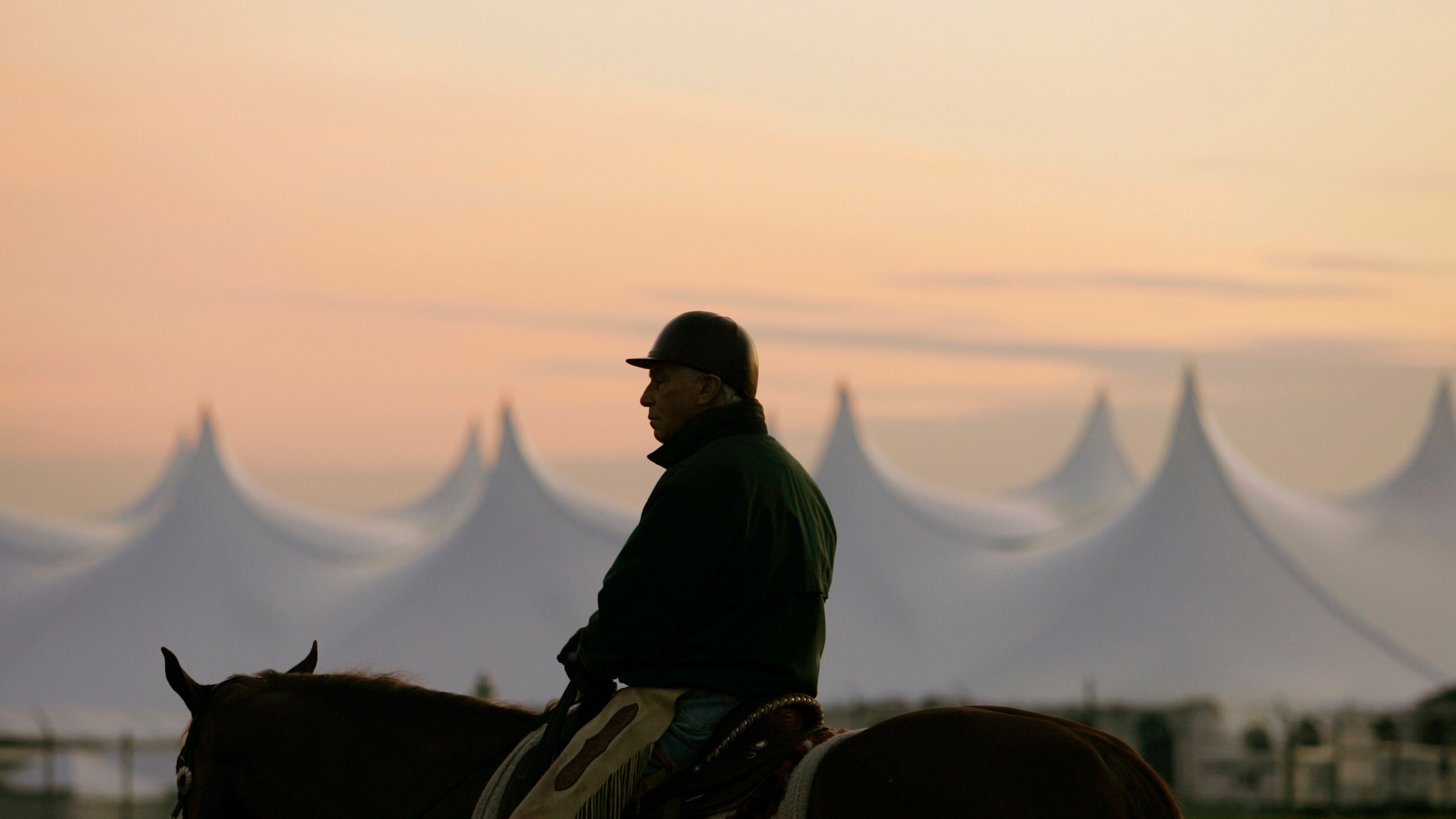 FILE - Trainer D. Wayne Lukas sits atop his horse as he watches morning workouts against the backdrop of a large tent set up in the infield before sunrise at Churchill Downs in Louisville, Ky., April 25, 2009. (AP Photo/Ed Reinke, file)