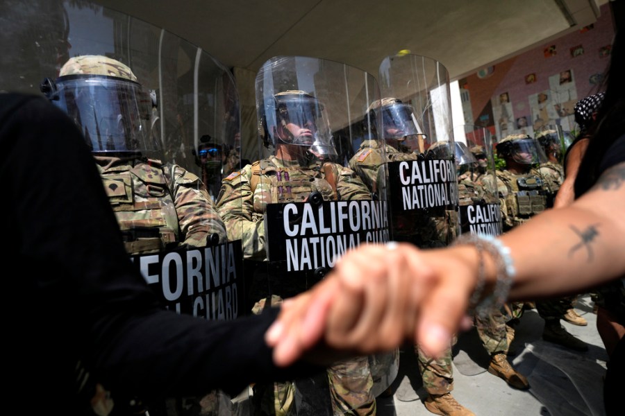 Protesters clasp hands in front of a line of California National Guardsmen