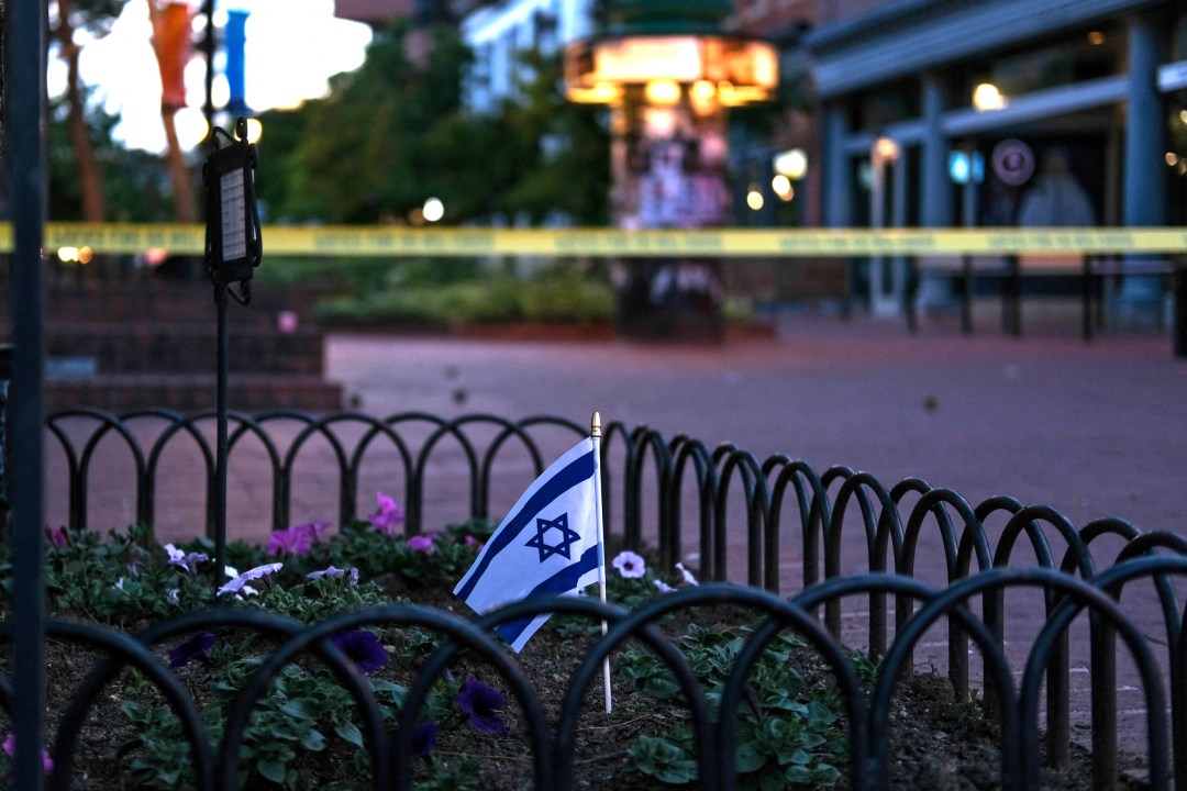 An Israeli flag stands in a bed of flowers as caution tape blocks off a street