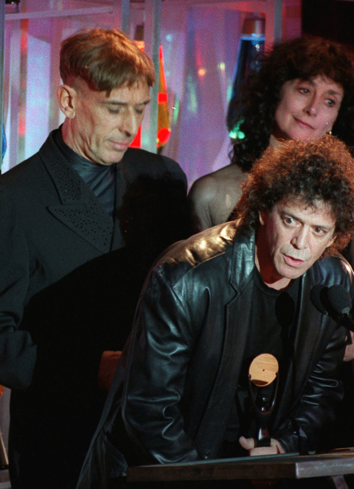 FILE - Lou Reed speaks at the podium, center, as he and his Velvet Underground band mates John Cale, left, and at Martha Morrison are inducted into the Rock and Roll Hall of Fame in New York on s Jan. 17, 1996. (AP Photo/Mark Lennihan, File)