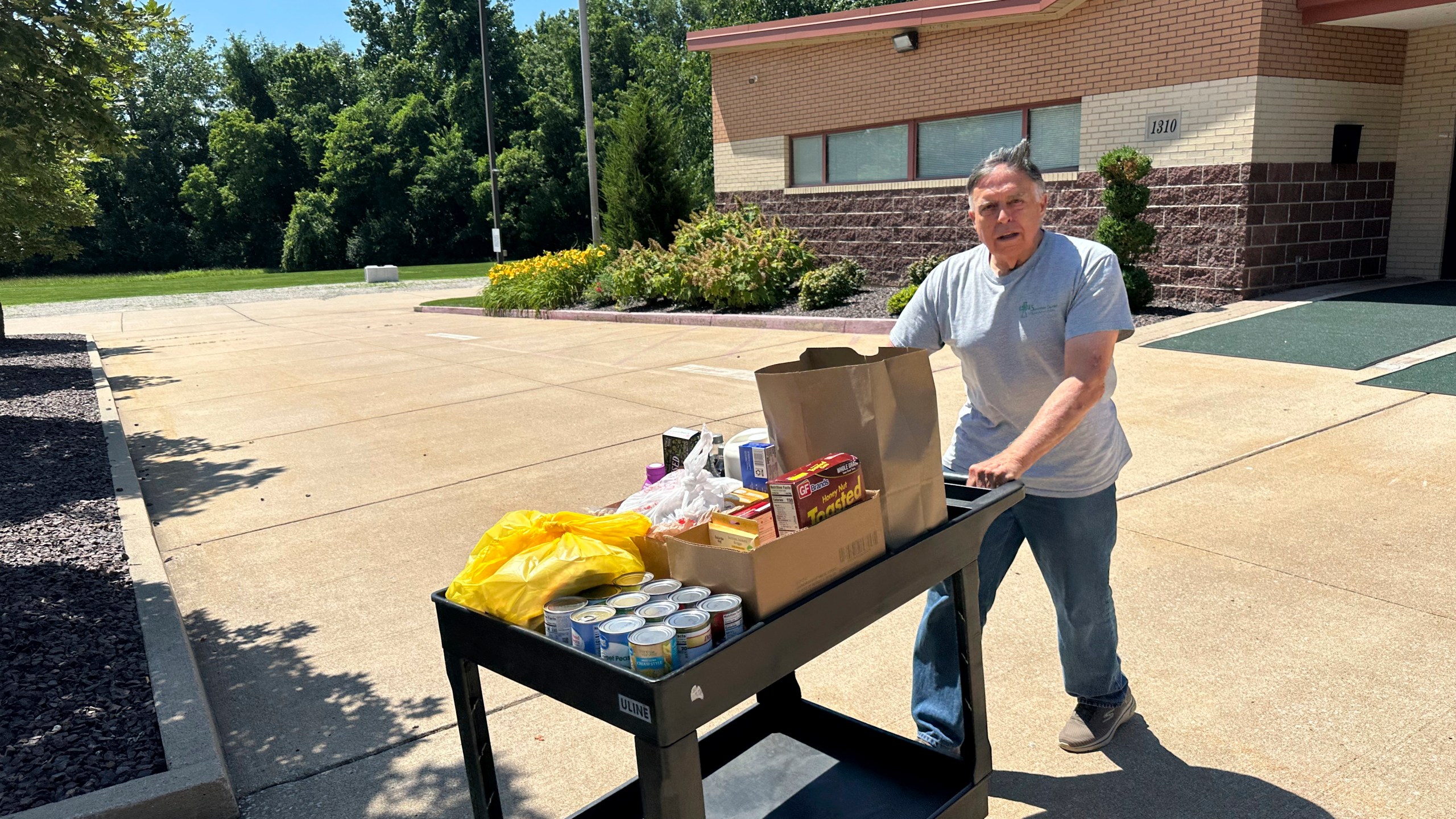Dick Hronick, a volunteer at the Samaritan Center food pantry in Jefferson City, Mo., pushes a cart of food across the parking lot for distribution to people on Tuesday, July 1, 2025. (AP Photo/David A. Lieb)