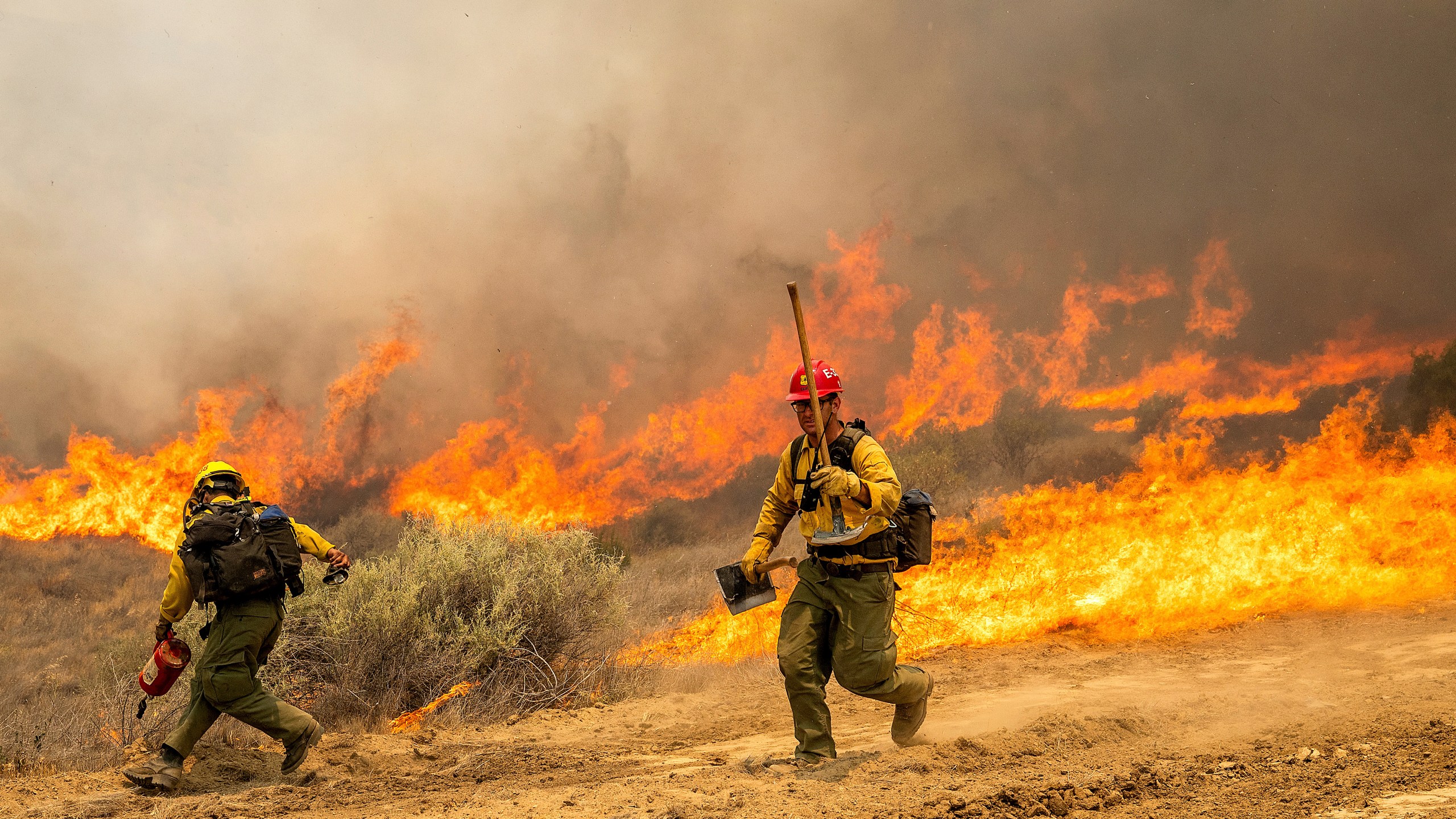 Firefighters scrambles to keep the Madre Fire from crossing a dozer line as it makes a run along Highway 166 on Thursday, July 3, 2025, in San Luis Obispo County, Calif. (AP Photo/Noah Berger)
