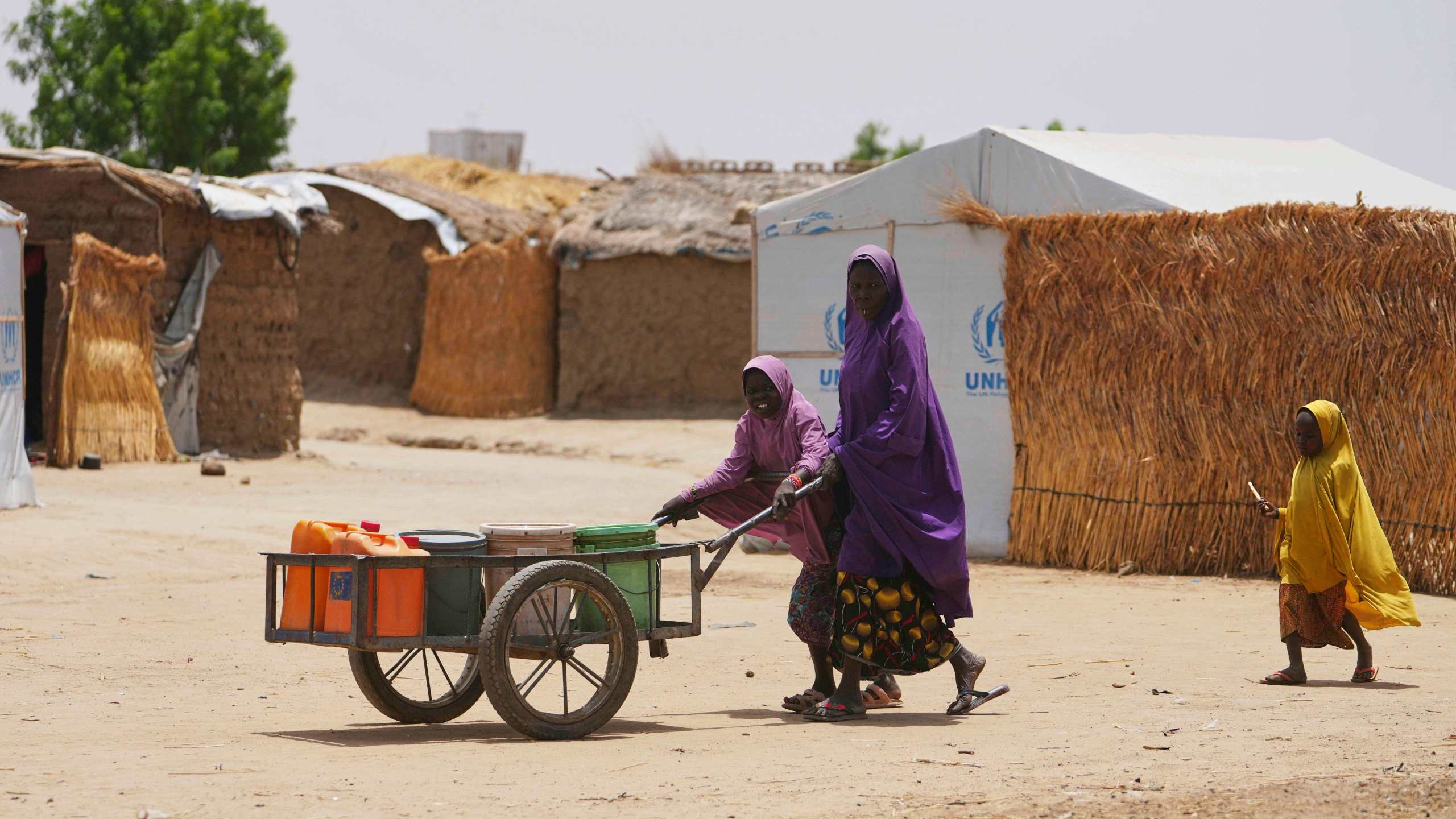 FILE - A woman and young girl displaced from Boko Haram attacks push a cart in Dikwa, Borno province, north east Nigeria, Tuesday, April 29, 2025. (AP Photo/Sunday Alamba, File)