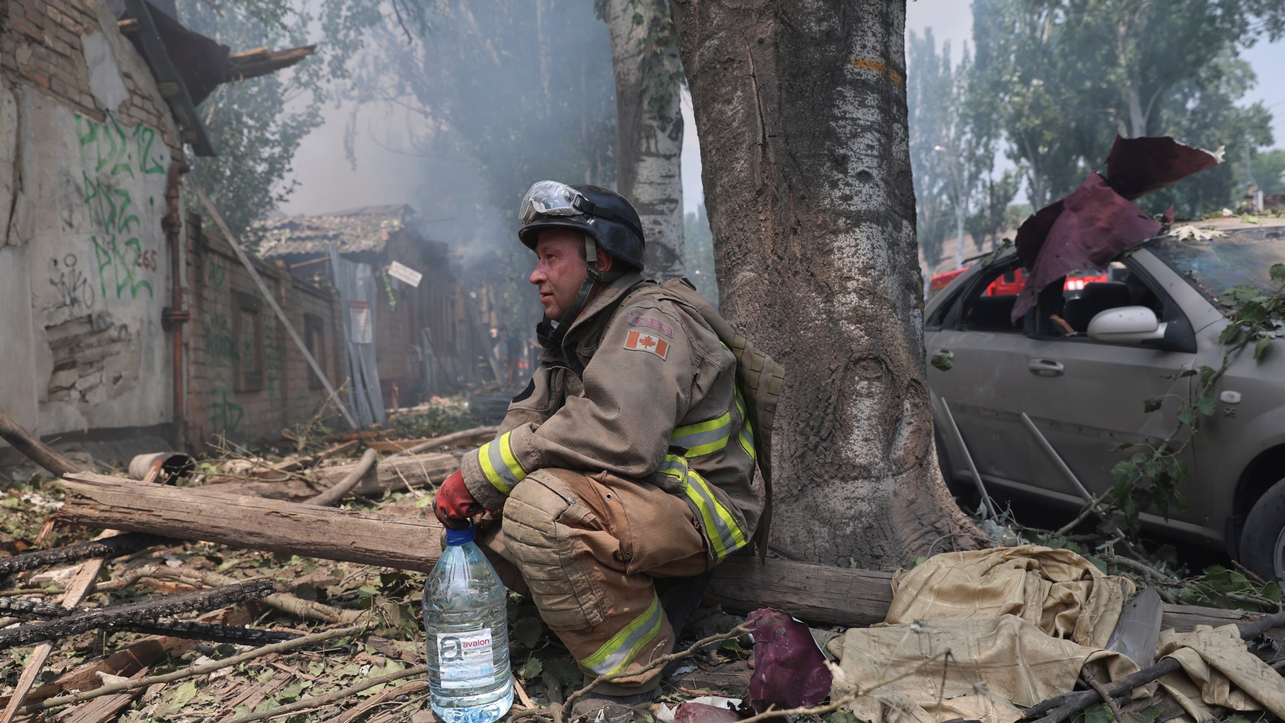 A rescue worker rests by a tree as others put out a fire
