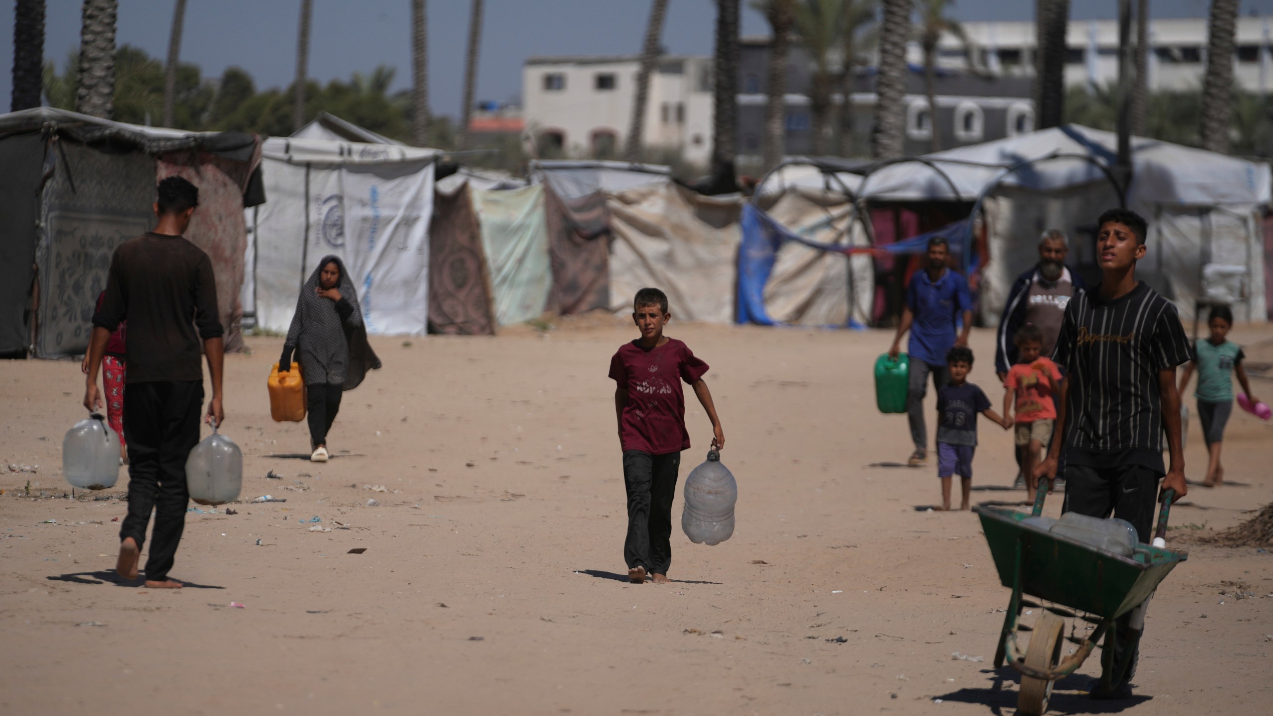 Palestinians carry containers for water at a camp for the displaced in Deir al-Balah, Gaza Strip, Monday, July 7, 2025. (AP Photo/Abdel Kareem Hana)