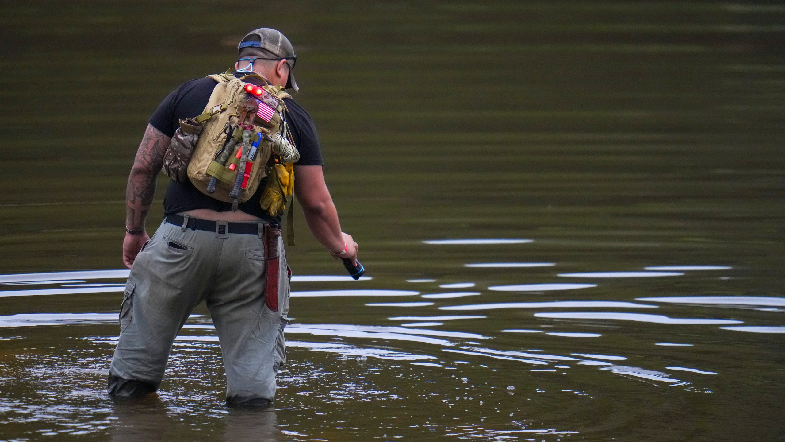 Avi Santos, 23, a civilian from San Antonio, Texas, wades the water at the Guadalupe River as he helps in the recovery effort near Camp Mystic, Sunday, July 6, 2025, in Hunt, Texas, after a flash flood swept through the area. (AP Photo/Julio Cortez)