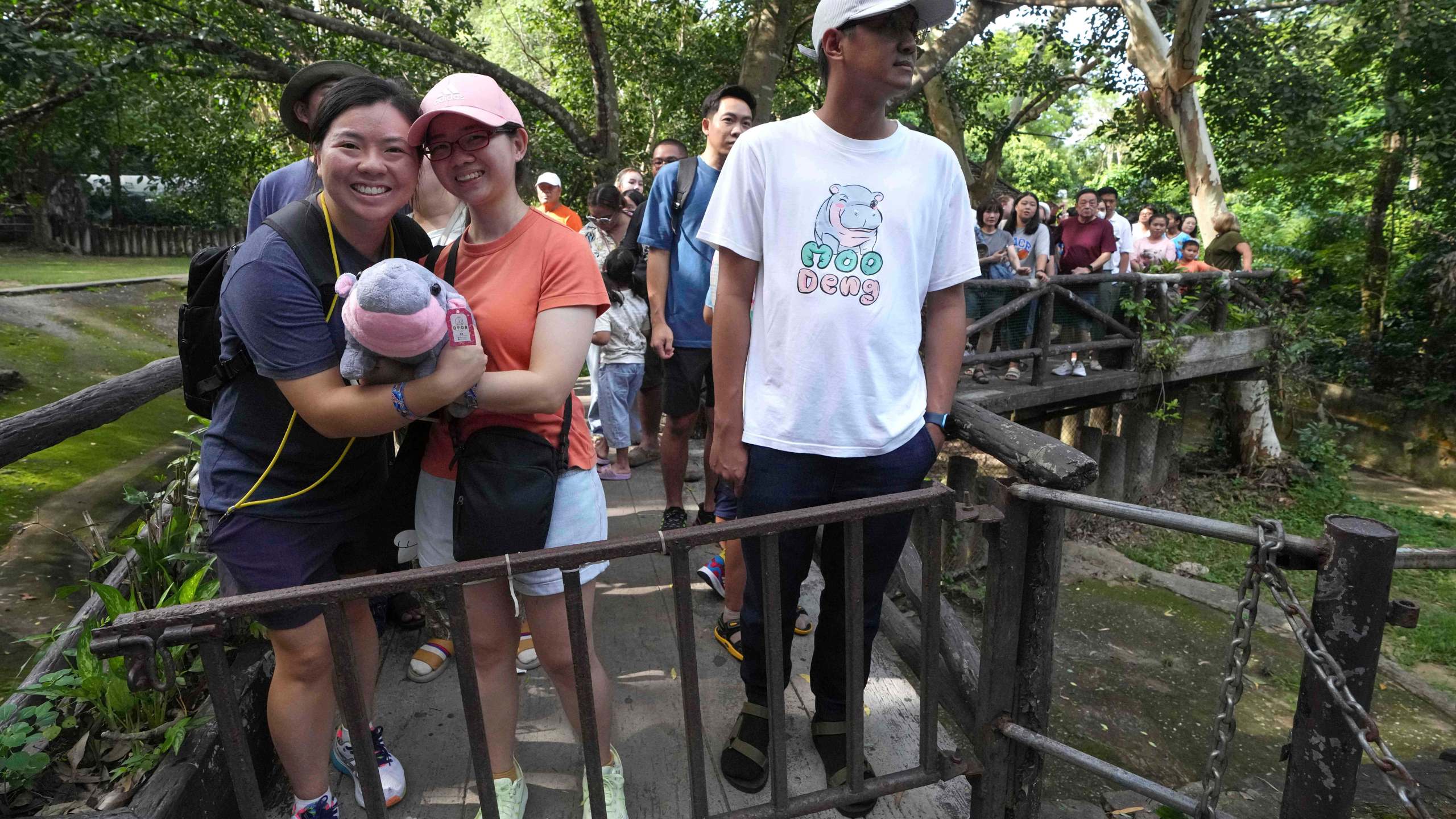 Visitors hold a soft toy of hippo Moo Deng as they lin up to watch Moo Deng, which turned one year old, at the Khao Kheow Open Zoo in Chonburi province, Thailand, Thursday, July 10, 2025. (AP Photo/Sakchai Lalit)
