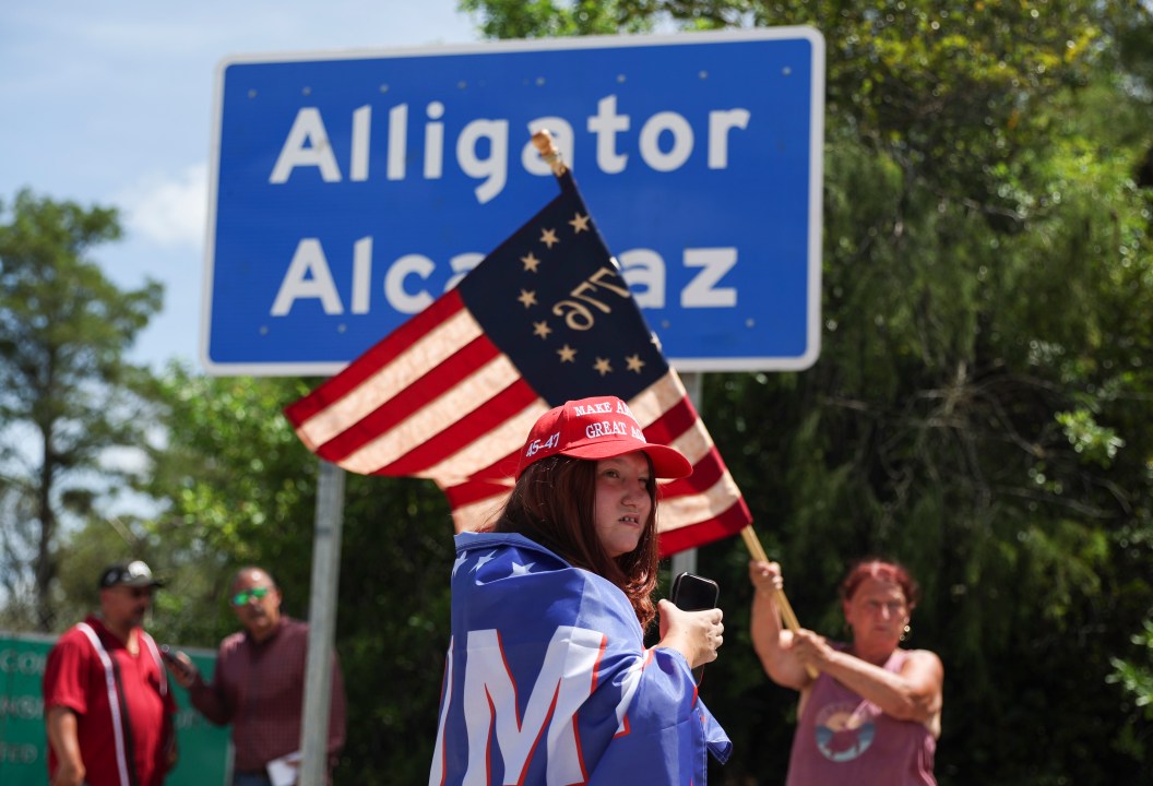 Dianne Mourer waves an American flag as Rana Mourer stands in front of a sign reading "Alligator Alcatraz" outside the Dade-Collier Training and Transition Facility, Saturday, July 12, 2025, in Ochopee, Fla. (AP Photo/Alexandra Rodriguez)
