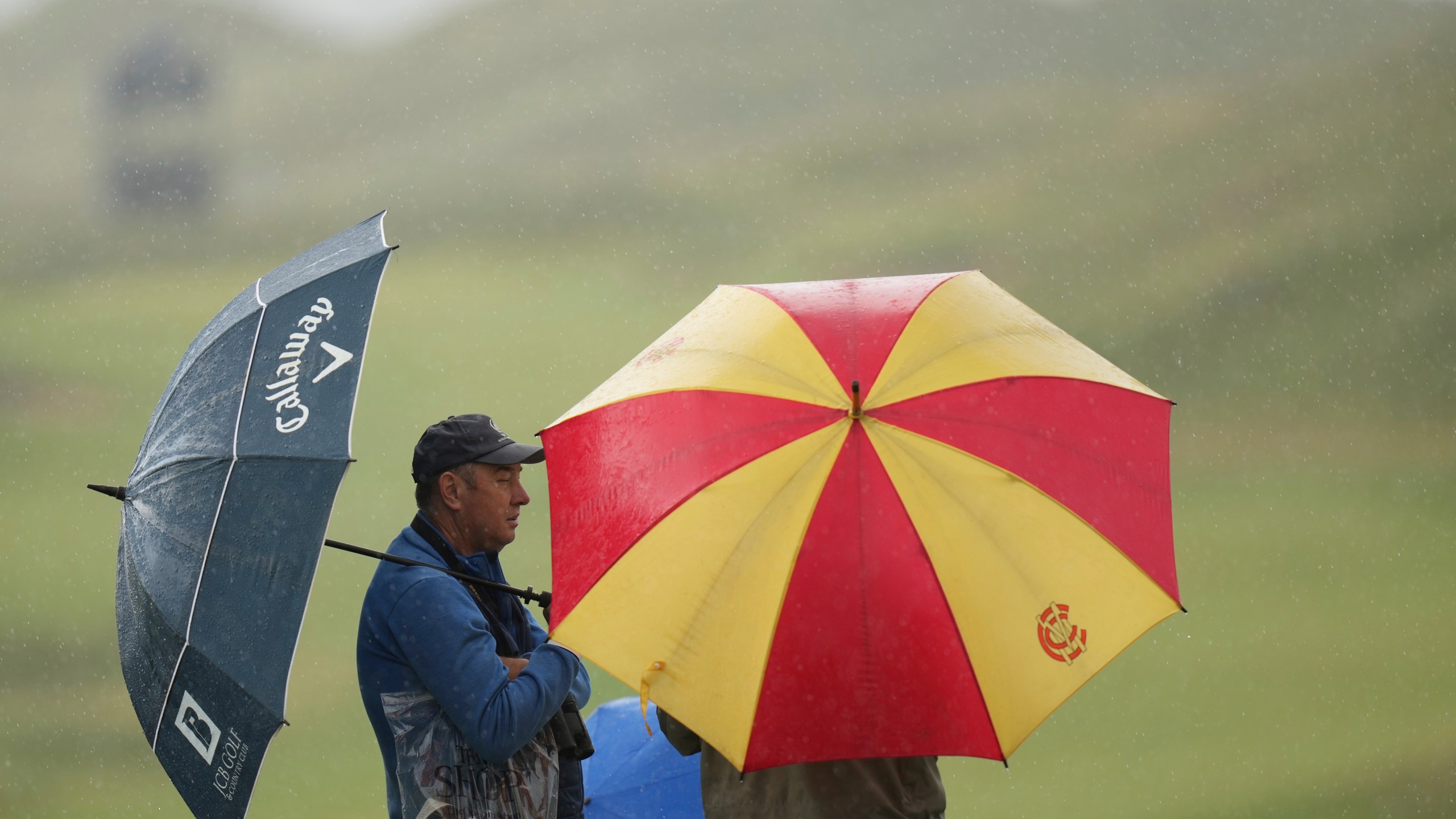 Spectators take cover under an umbrellas as play is suspended due to a thunderstorm waring during a practice round for the 2025 British Open golf championship at the Royal Portrush Golf Club, Northern Ireland, Monday, July 14, 2025. (AP Photo/Francisco Seco)