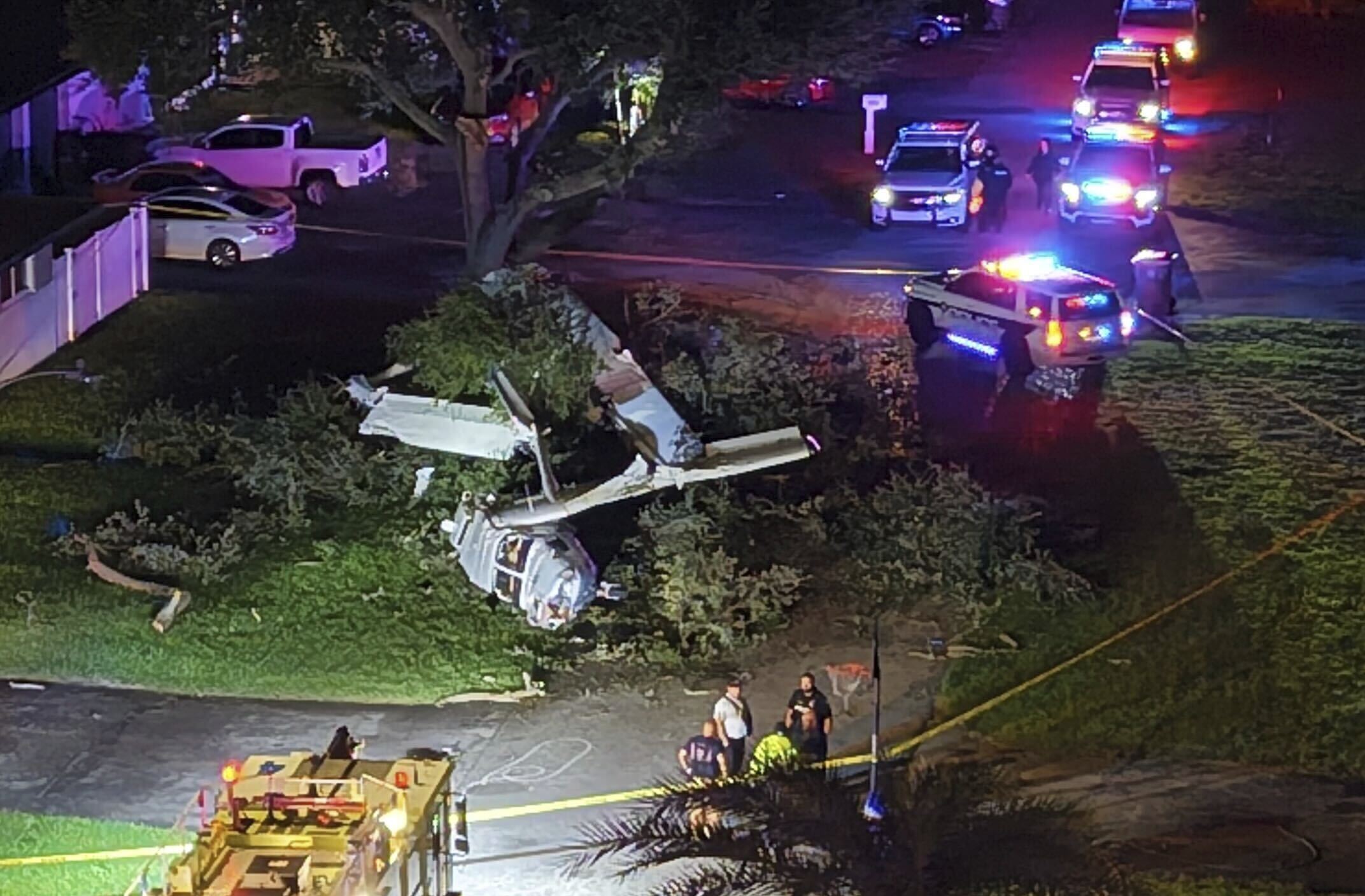 Emergency personnel work at the scene of the wreckage following a plane crash in a yard in the Pines Village community in Pembroke Pines, Fla., Sunday night, July 13, 2025. The pilot and three passengers escaped with only minor injuries after a group of good Samaritans rushed in to free them. (Joe Cavaretta/South Florida Sun-Sentinel via AP)