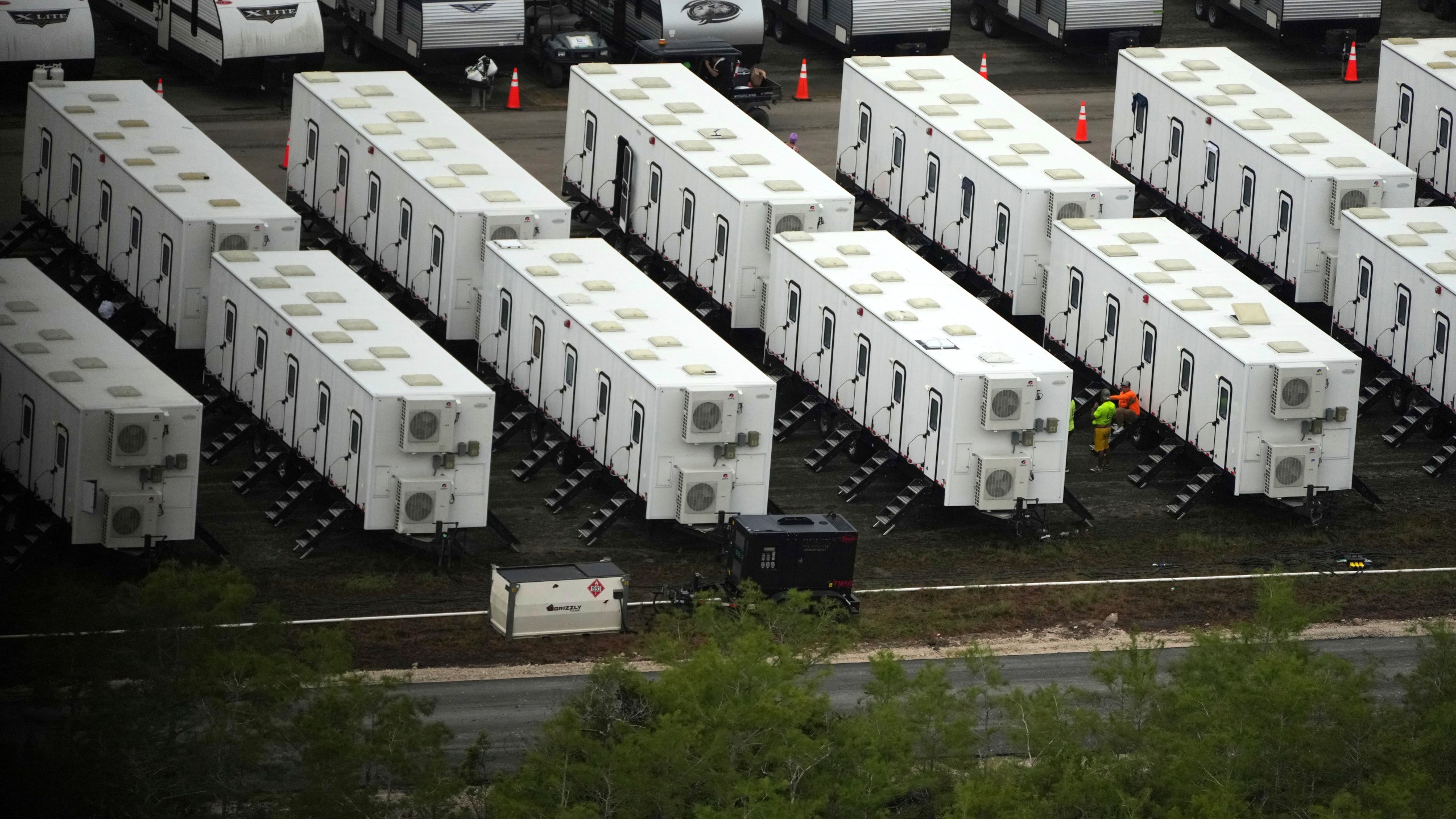 Workers sit alongside trailers as work progresses on a new migrant detention center dubbed "Alligator Alcatraz," at Dade-Collier Training and Transition facility in the Florida Everglades, Friday, July 4, 2025, in Ochopee, Fla. (AP Photo/Rebecca Blackwell)