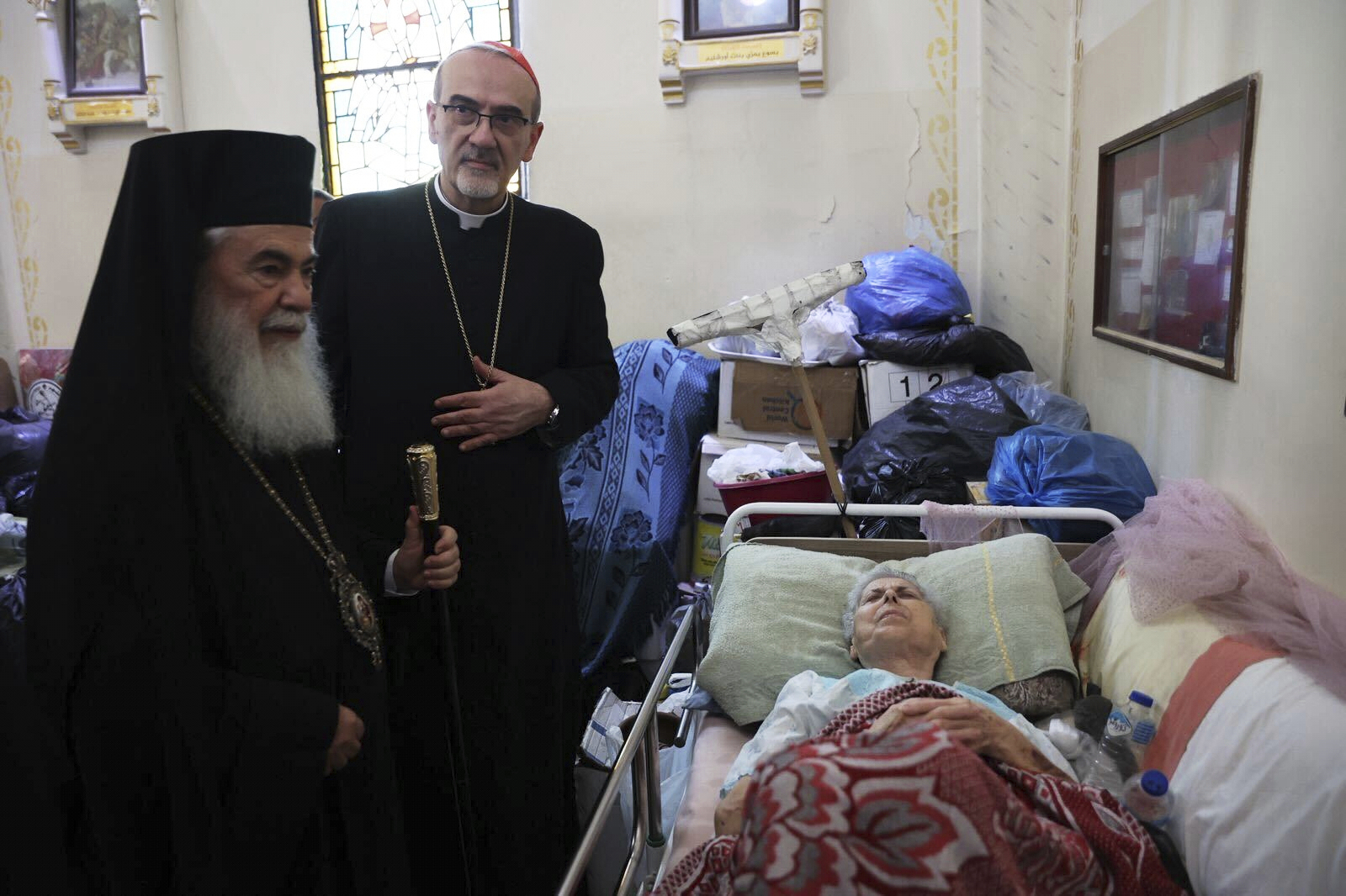 Patriarchs from Jerusalem, Greek Orthodox Patriarch Theophilos III, left, and Latin Patriarch Cardinal Pierbattista Pizzaballa, center, visit a wounded woman as they lead a religious delegation to the Gaza Strip at the Holy Family Catholic Church, struck by an Israeli shell the day before in Deir al-Balah, Friday, July 18, 2025. (Latin Patriarchate of Jerusalem via AP)