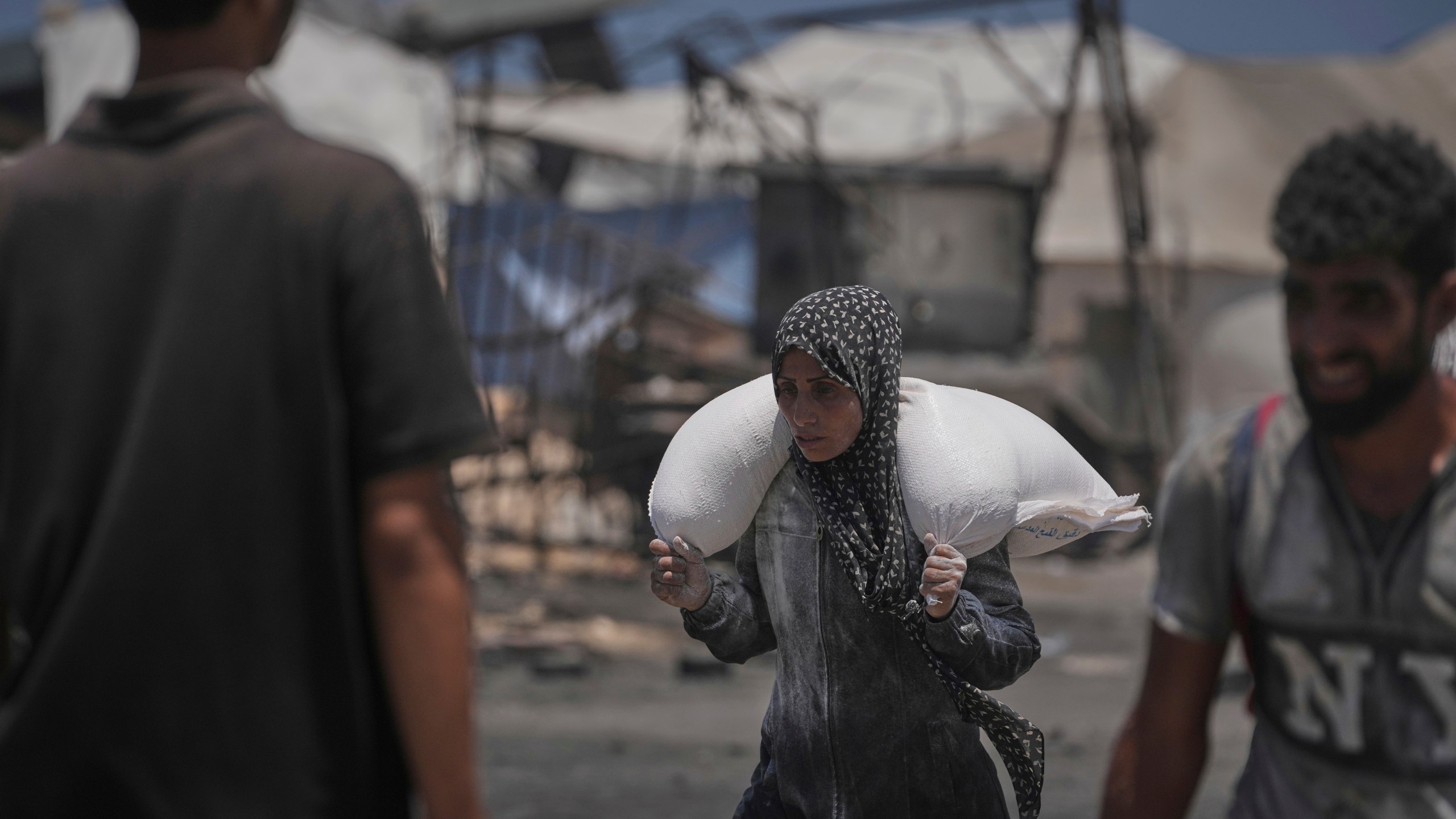 Palestinians carry sacks of flour unloaded from a humanitarian aid convoy that reached Gaza City from the northern Gaza Strip, Tuesday, July 22, 2025. (AP Photo/Jehad Alshrafi)