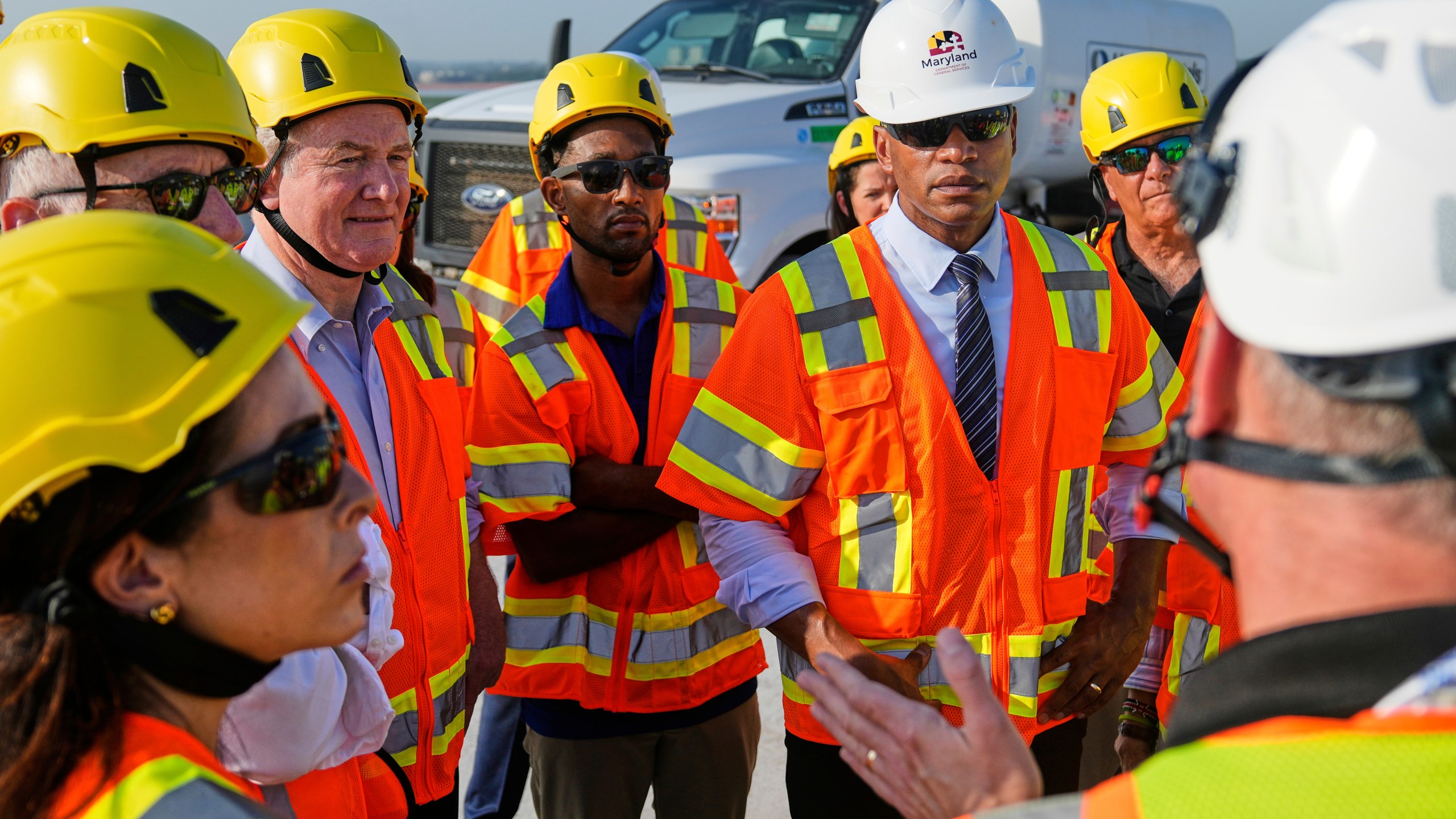 From center left, Sen. Chris Van Hollen, D-Md., Baltimore Mayor Brandon Scott and Maryland Gov. Wes Moore speak with representatives of the Maryland Transportation Authority during a tour of the demolition work zone for the remaining portions of the Francis Scott Key Bridge, Wednesday, July 30, 2025, in Baltimore. (AP Photo/Stephanie Scarbrough)