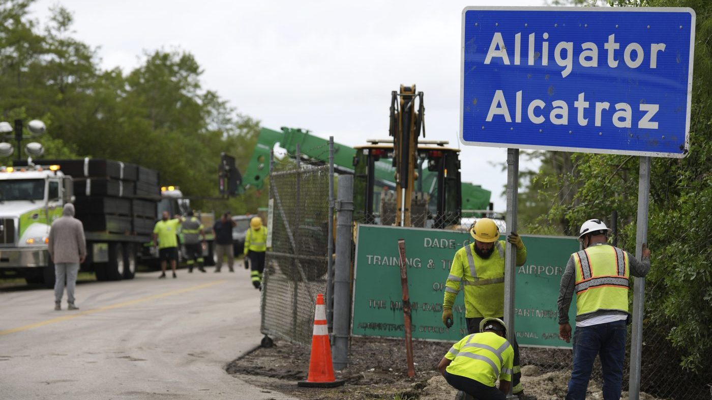 Workers install a sign reading "Alligator Alcatraz"