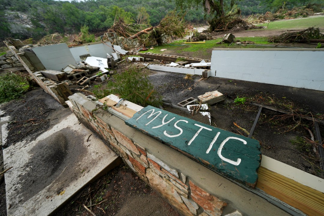 A Camp Mystic sign is seen surrounded by flooding debris