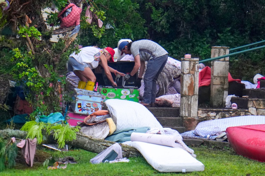 Two adults sweep through the belongings of campers in the aftermath of the flash flood