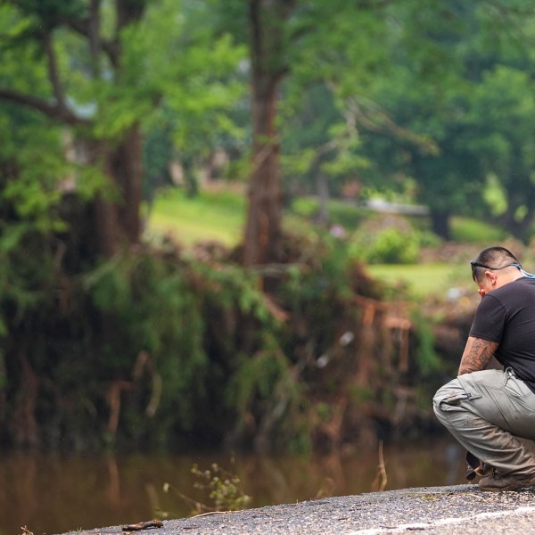 a person kneels on the roadside with their head in their hands