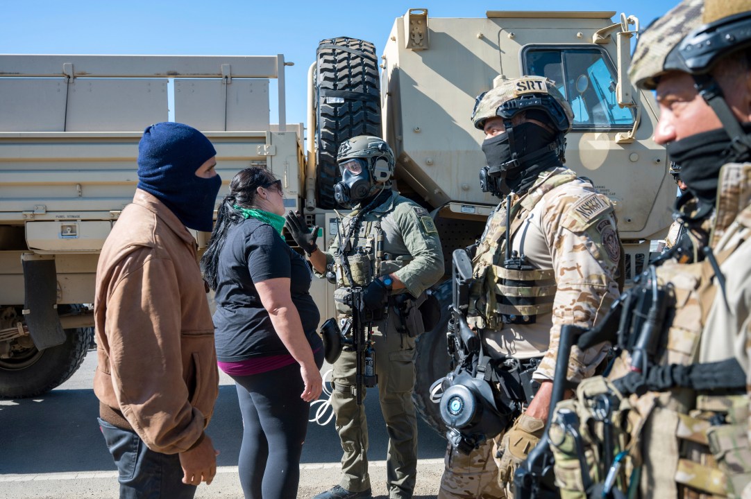 Federal immigration agents talk to Rebecca Torres, second left, after she tried to block a military vehicle during a raid in the agriculture area of Camarillo, Calif., Thursday, July 10, 2025
