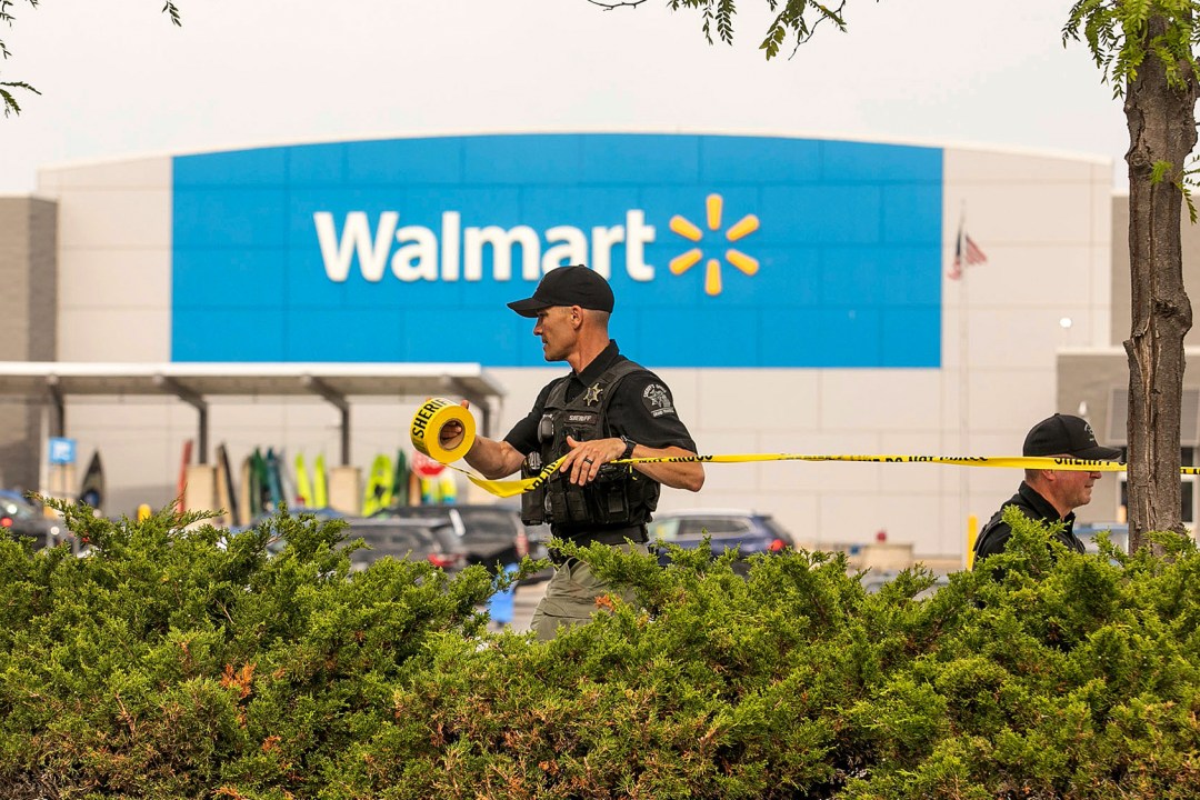 Police officer unrolling yellow security tape in front of Walmart sign