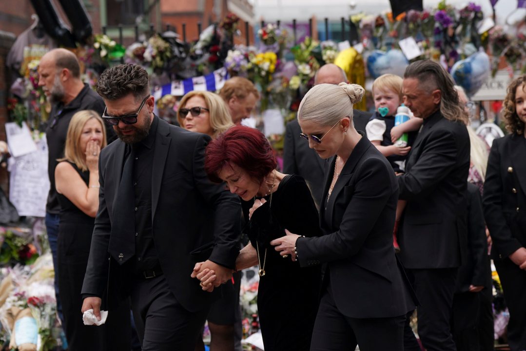 The family of Ozzy Osbourne react as they lay and view the flowers left at the Black Sabbath Bridge bench on Broad Street in memory of Black Sabbath frontman Ozzy Osbourne ahead of his funeral procession, in Birmingham, England, Wednesday July 30, 2025. (Joe Giddens/PA via AP)