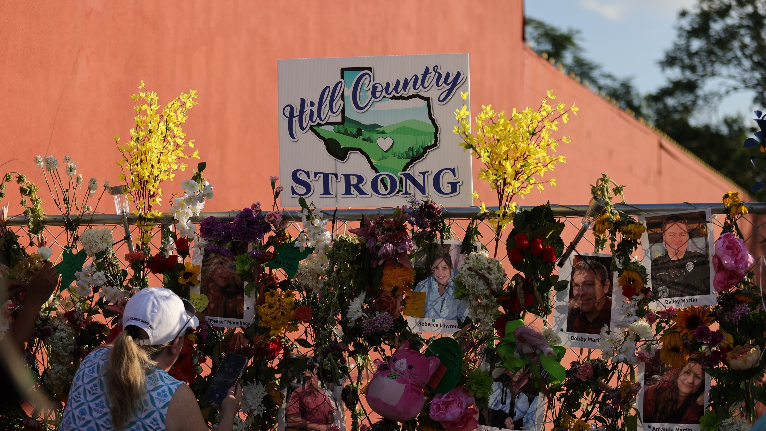 a crowd gathers at a vigil with photos of victims in front of a sign reading HILL COUNTRY STRONG
